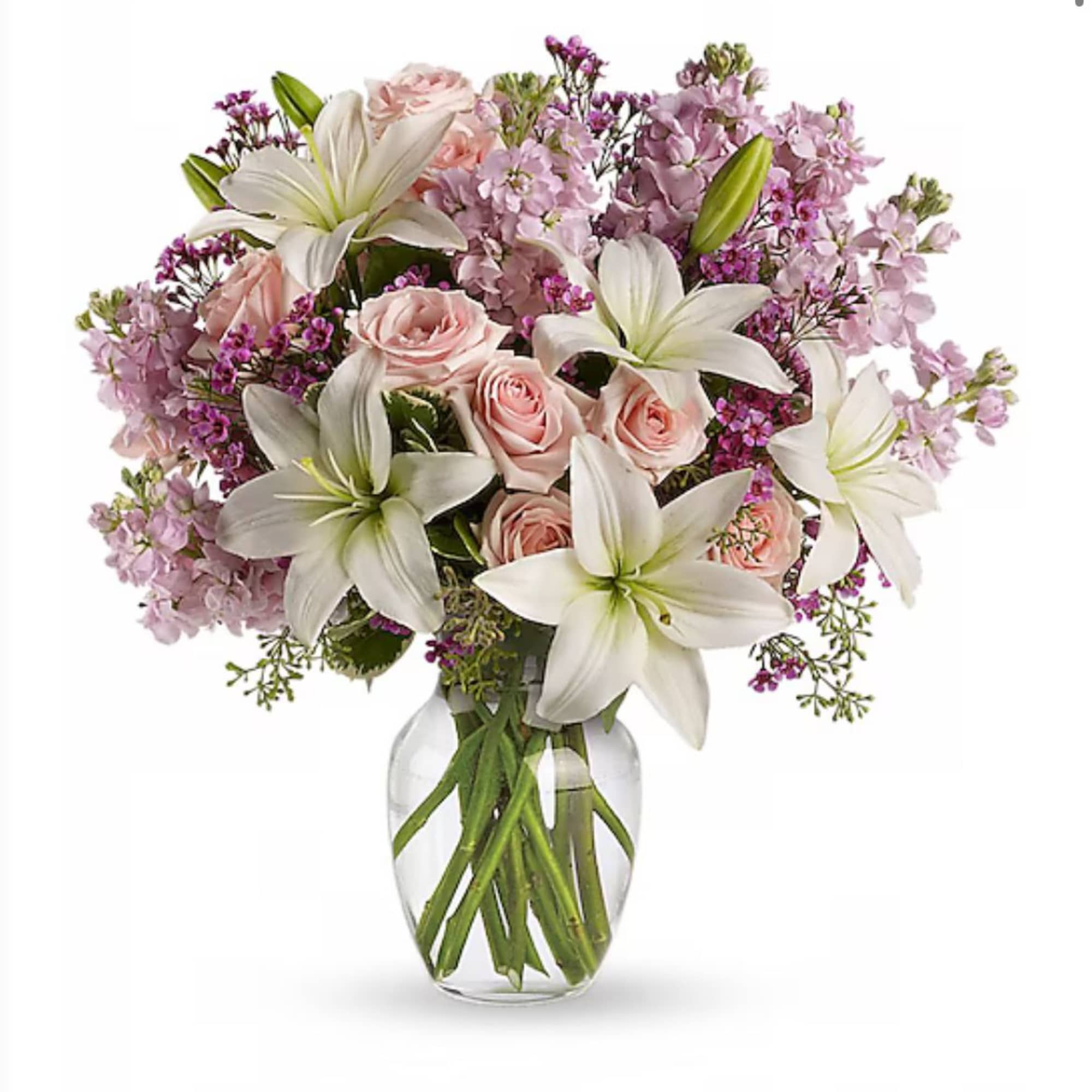 Arrangement of white lilies, pink roses, and lavender flowers in a clear glass vase