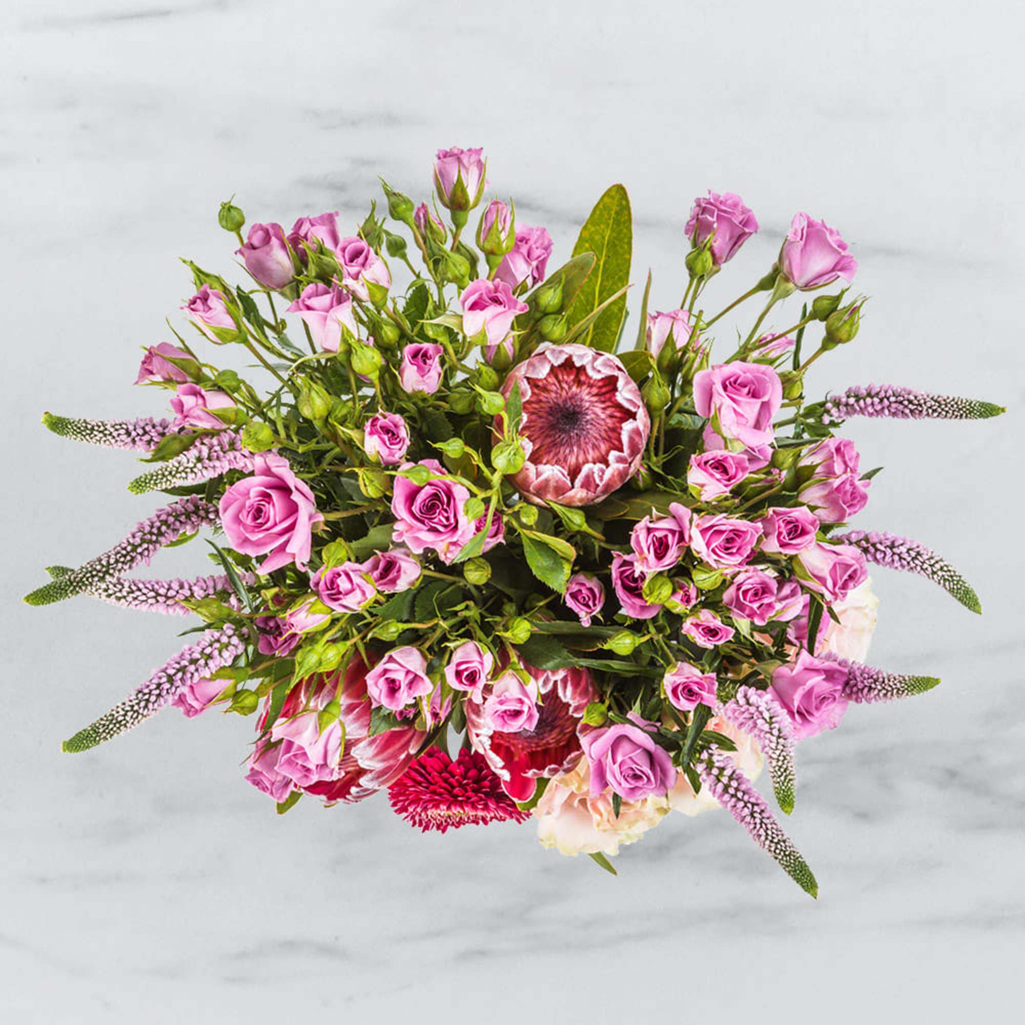 Top view of a lush arrangement of pink spray roses and protea blooms in a rounded bouquet