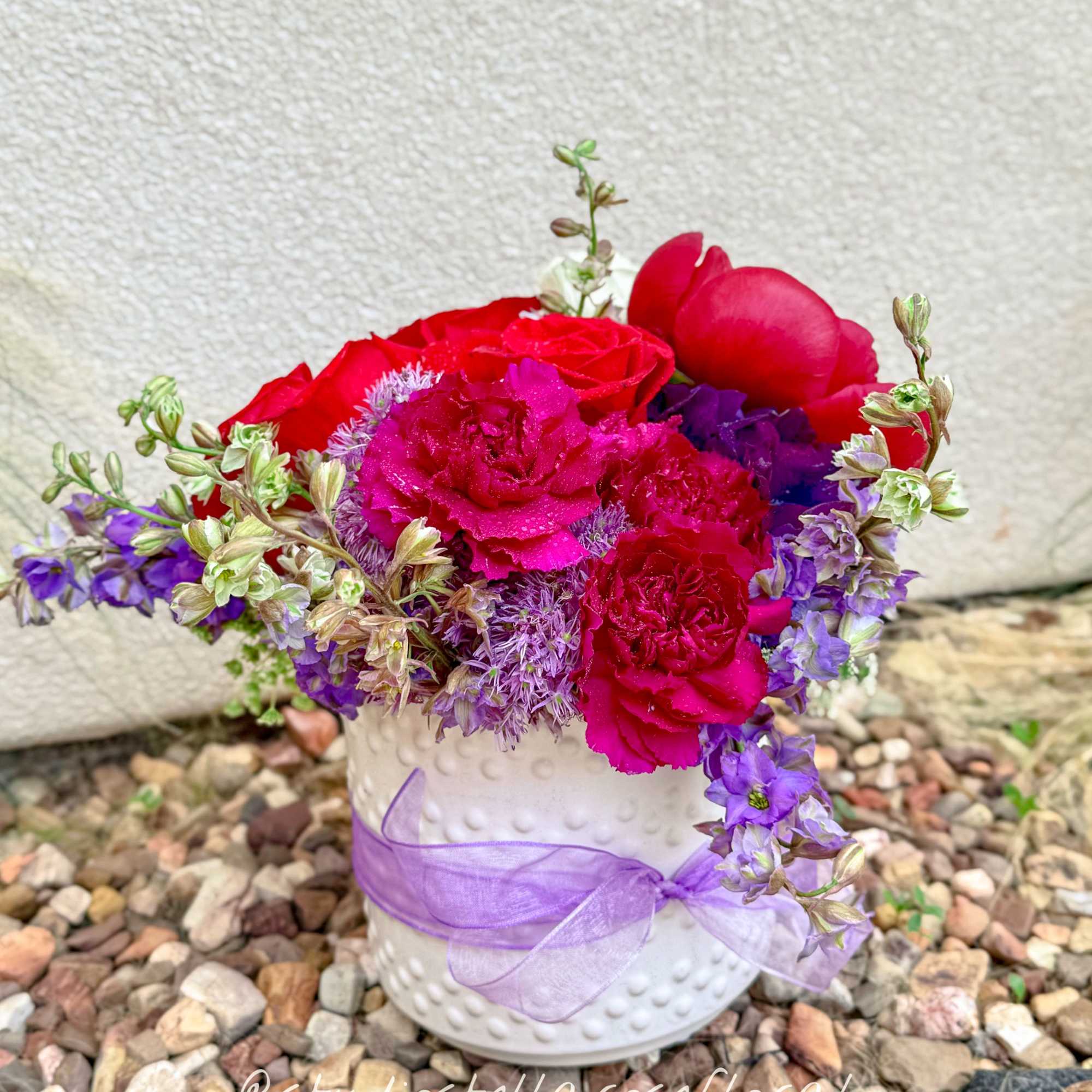Pink and purple flowers arranged in a white vase with a lavender ribbon.