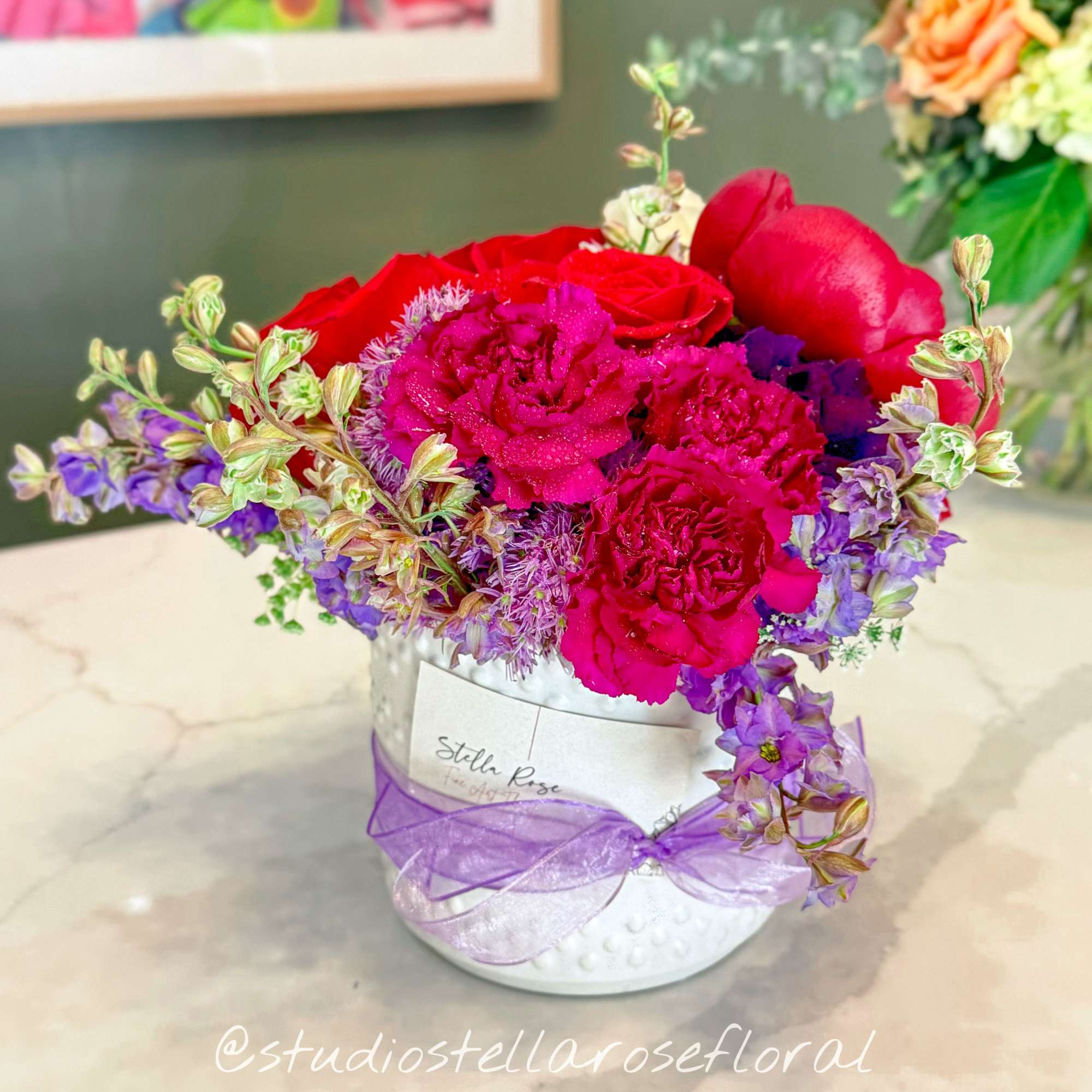 Pink and red floral arrangement in a white hat box with a purple ribbon