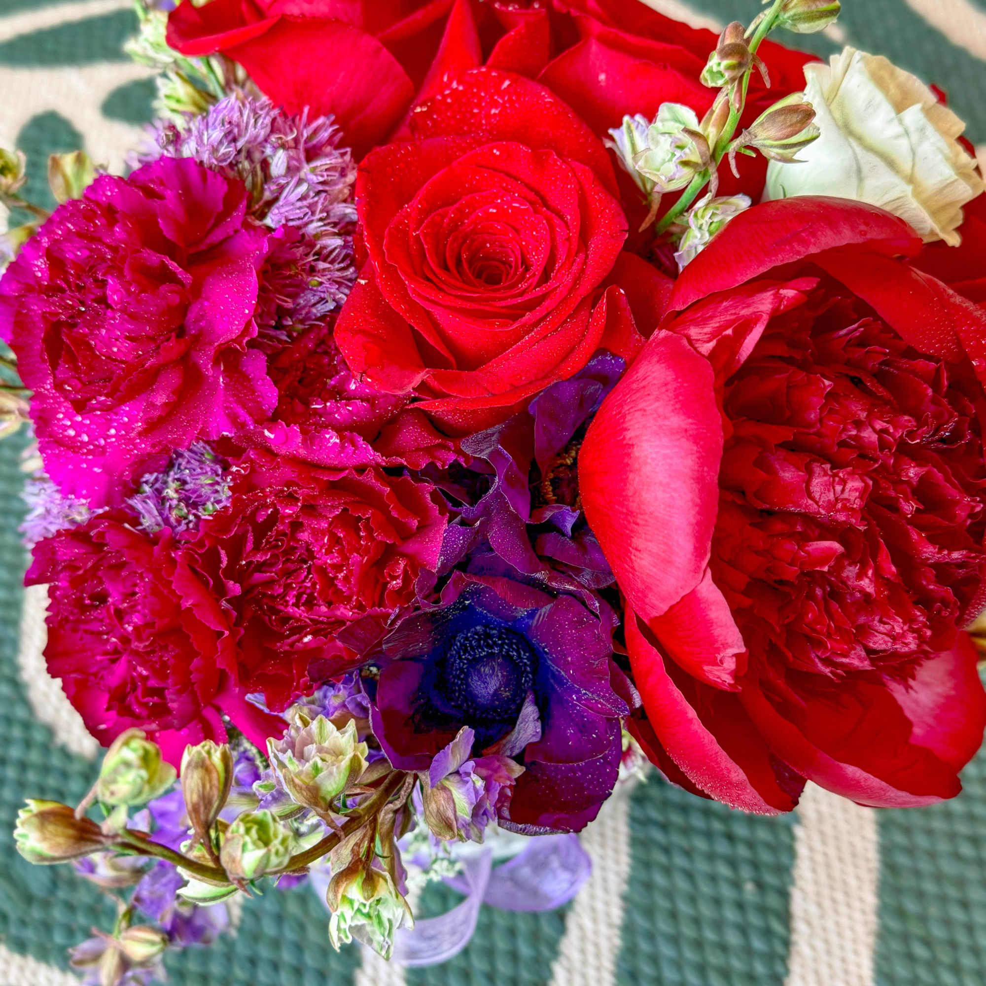 Close-up bouquet of red roses, pink carnations, and purple flowers