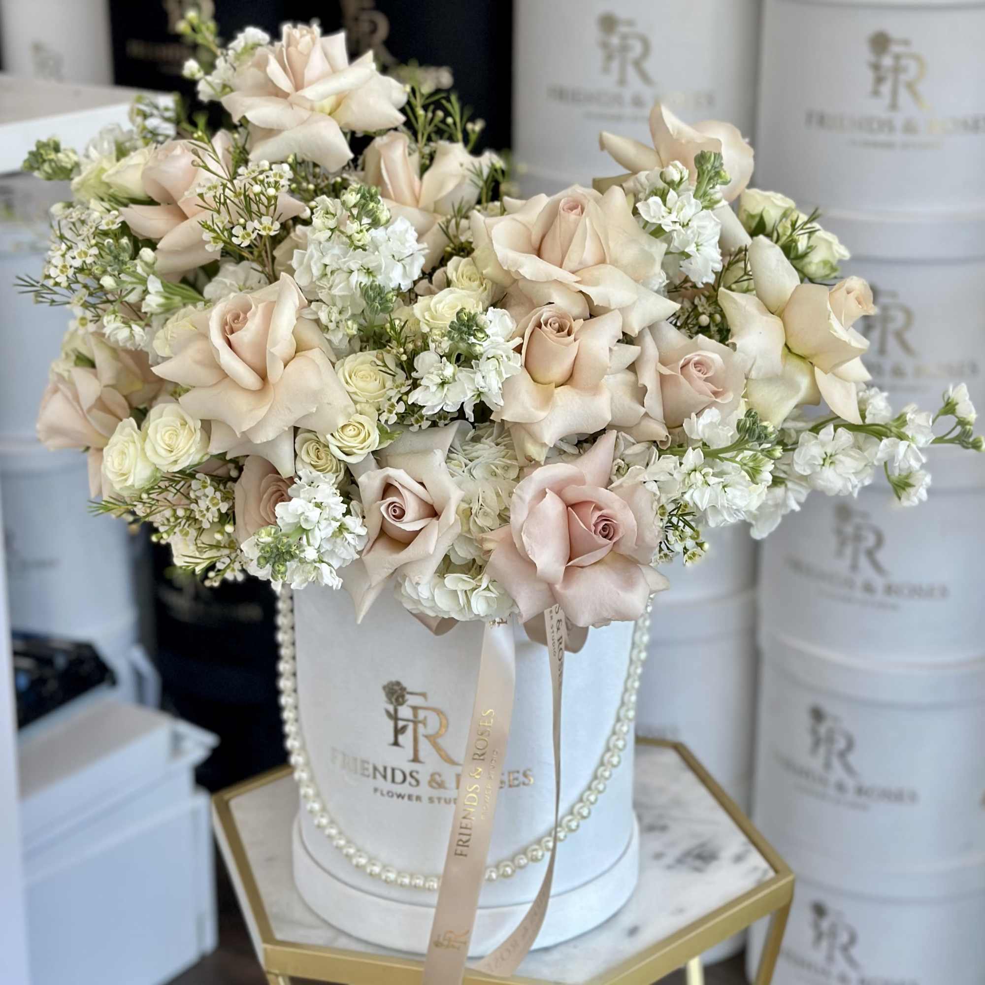 Blush roses and white flowers arranged in a white hatbox