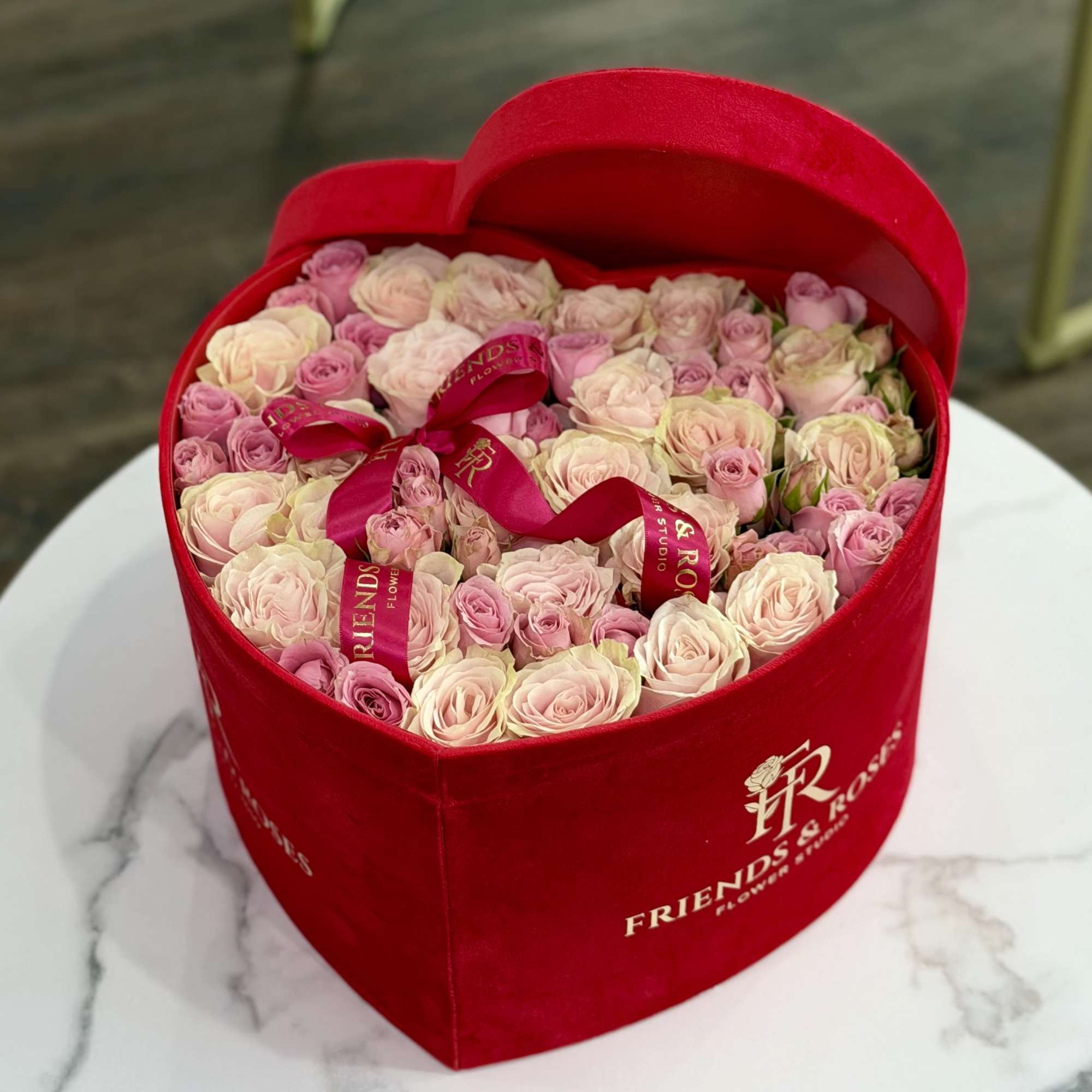 Pink and cream roses arranged in a red heart-shaped box