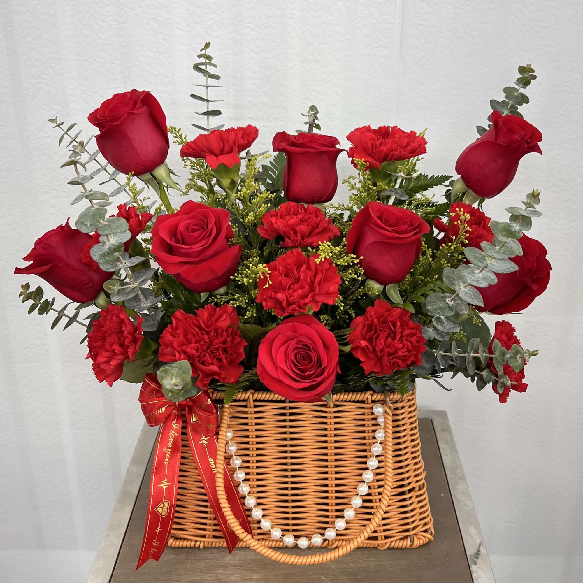 A charming basket arrangement featuring fresh red roses and carnations, accented with