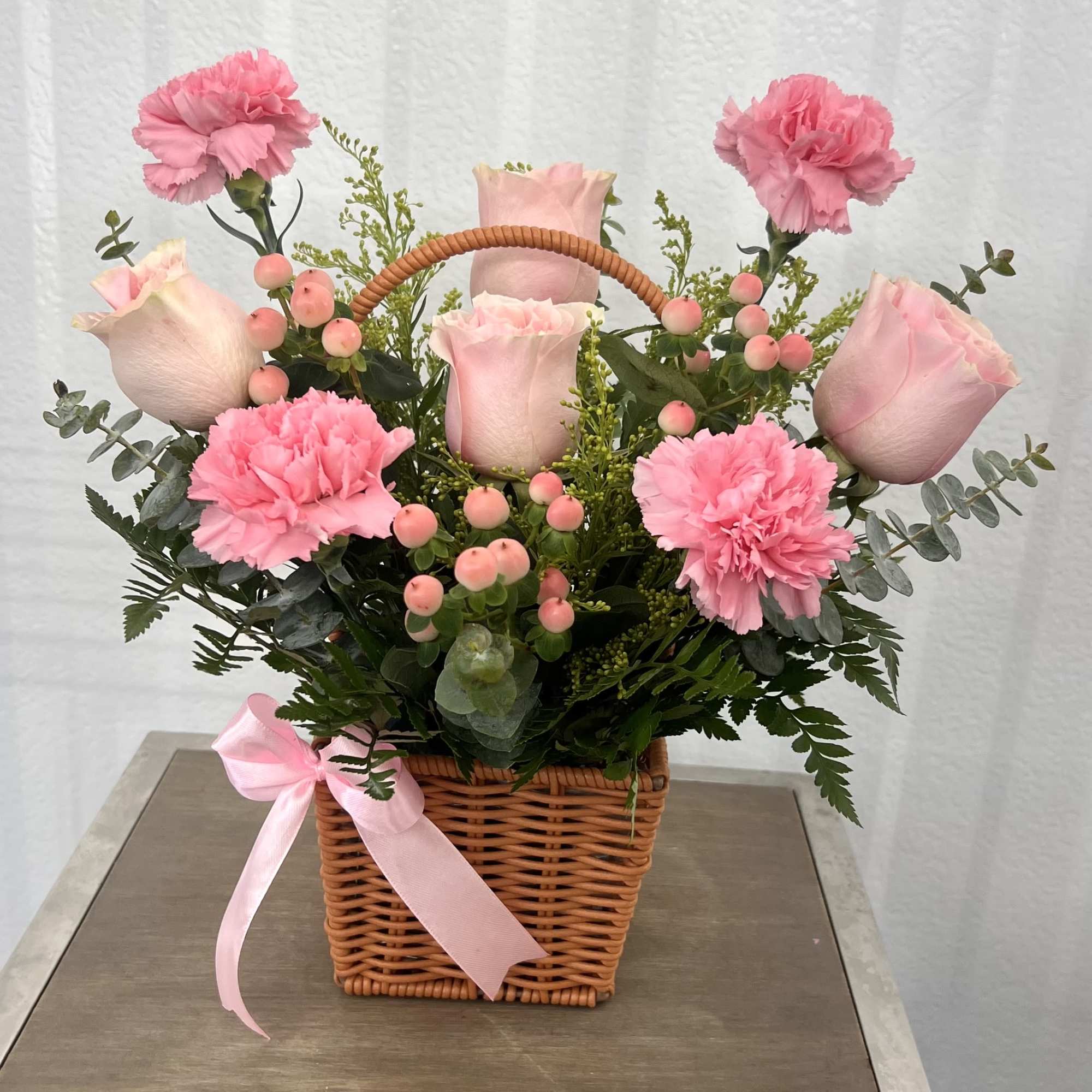 A soft and elegant basket arrangement with blush pink roses, carnations, and