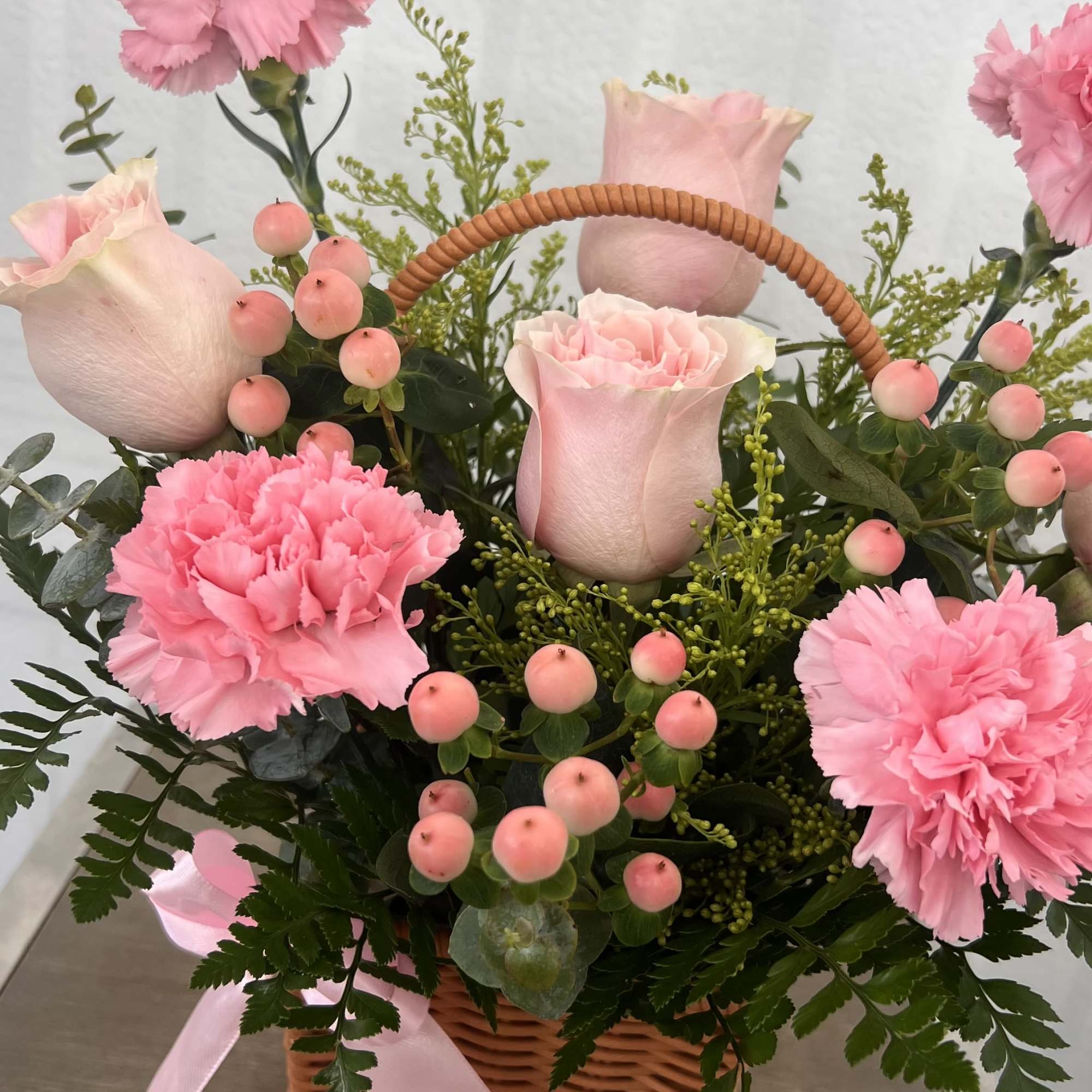 A soft and elegant basket arrangement with blush pink roses, carnations, and