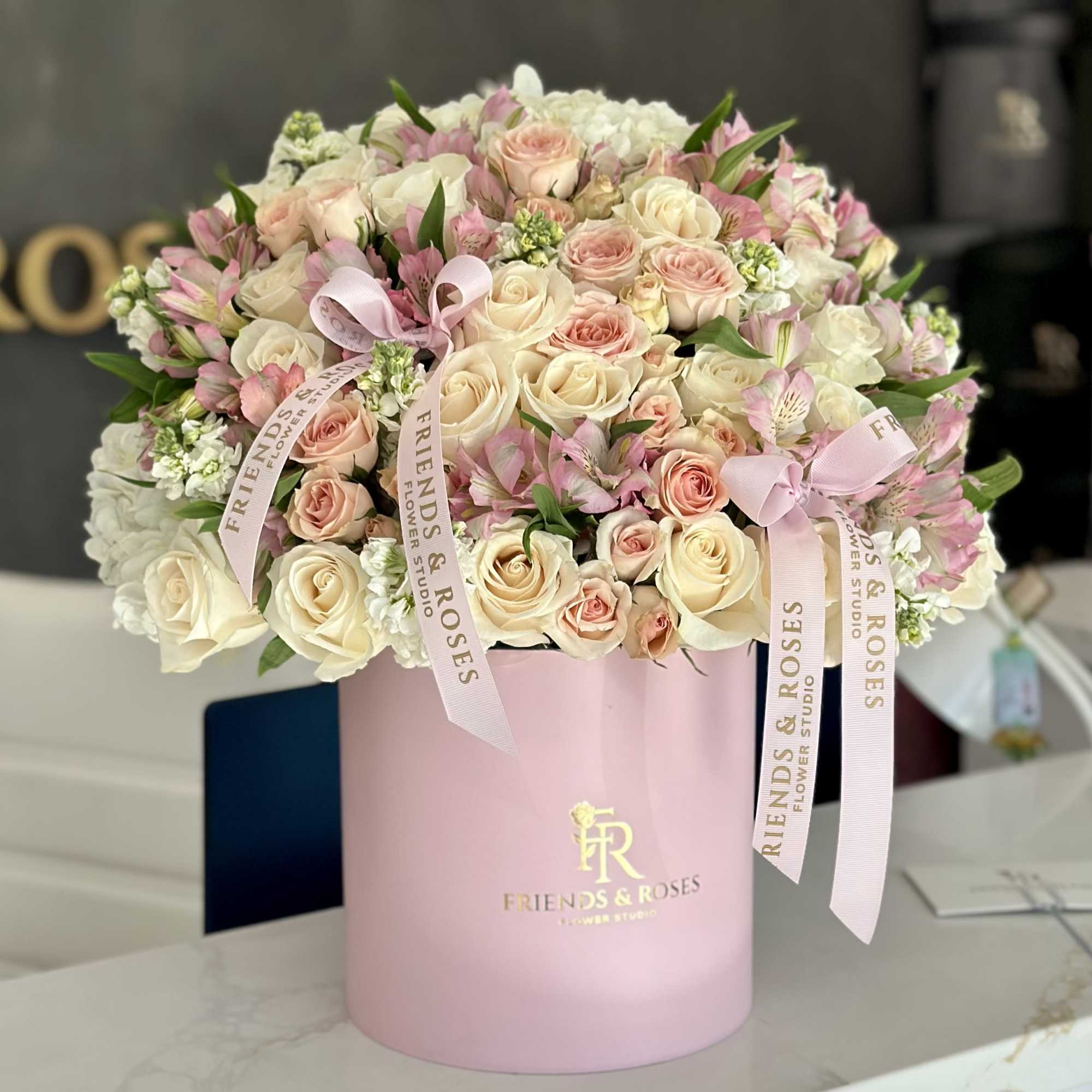 Pink and cream roses arranged in a pink hat box with ribbons
