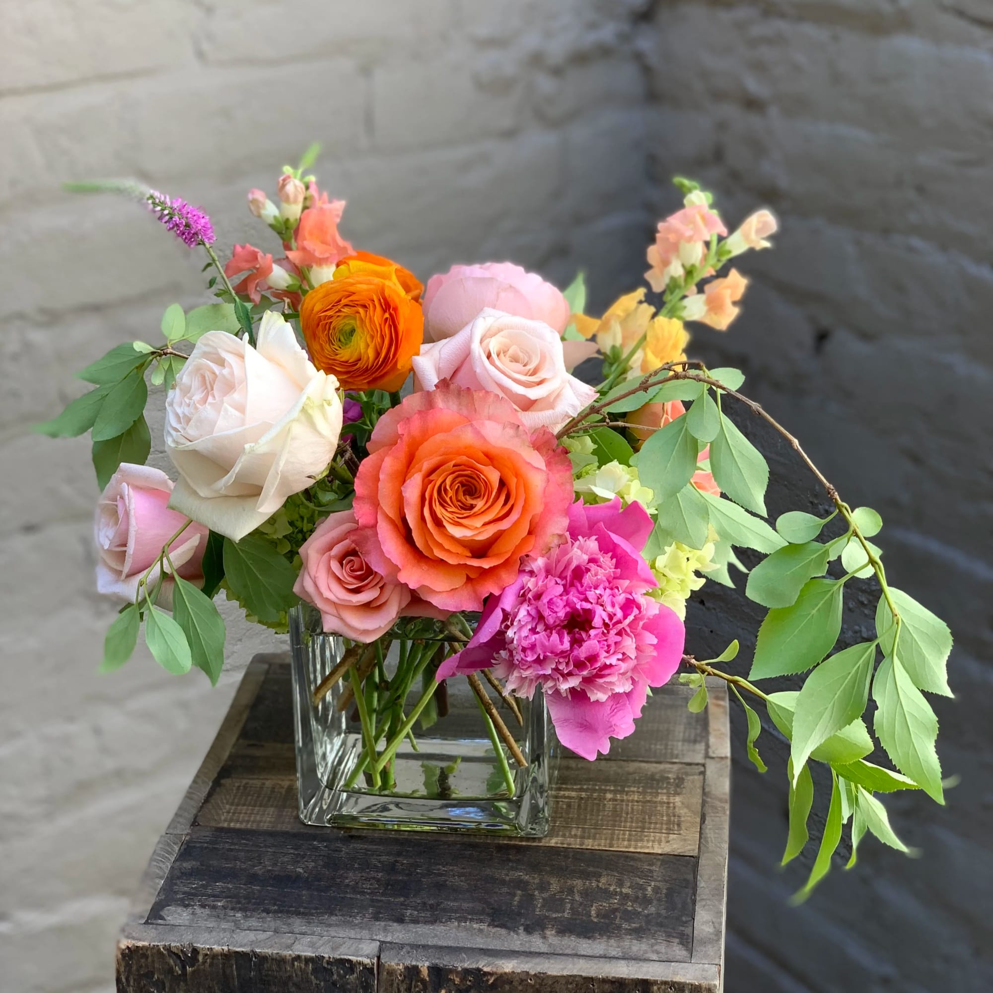 Mixed bouquet of roses and other blooms in a clear square vase