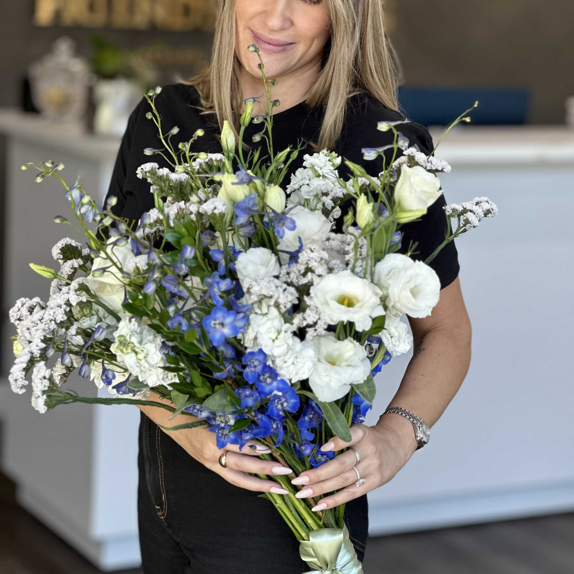 Woman holding a large bouquet of white and blue flowers tied with a satin ribbon.