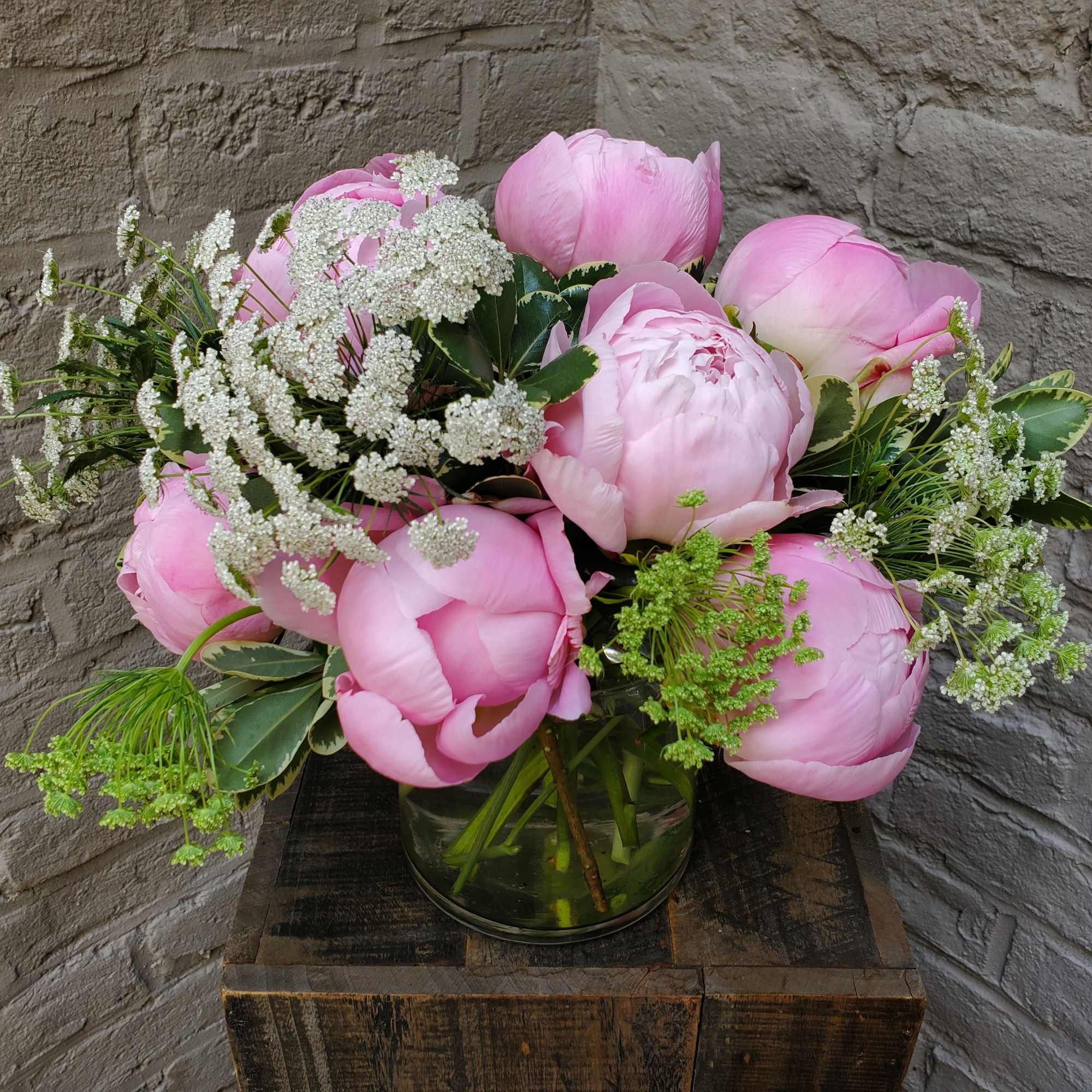 Pink peonies and white filler flowers in a clear glass vase