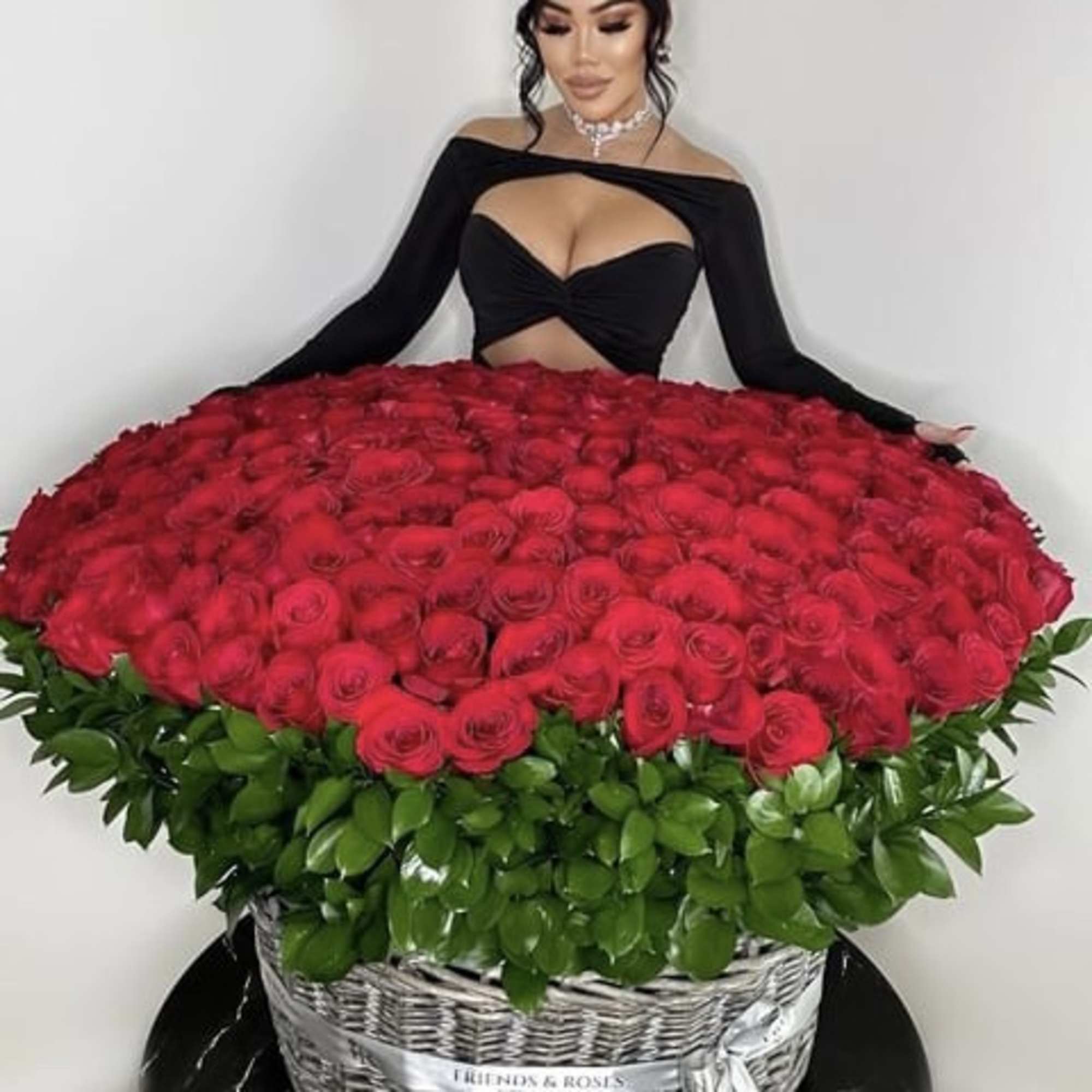 Large basket of red roses with green foliage, held by a woman in a black dress