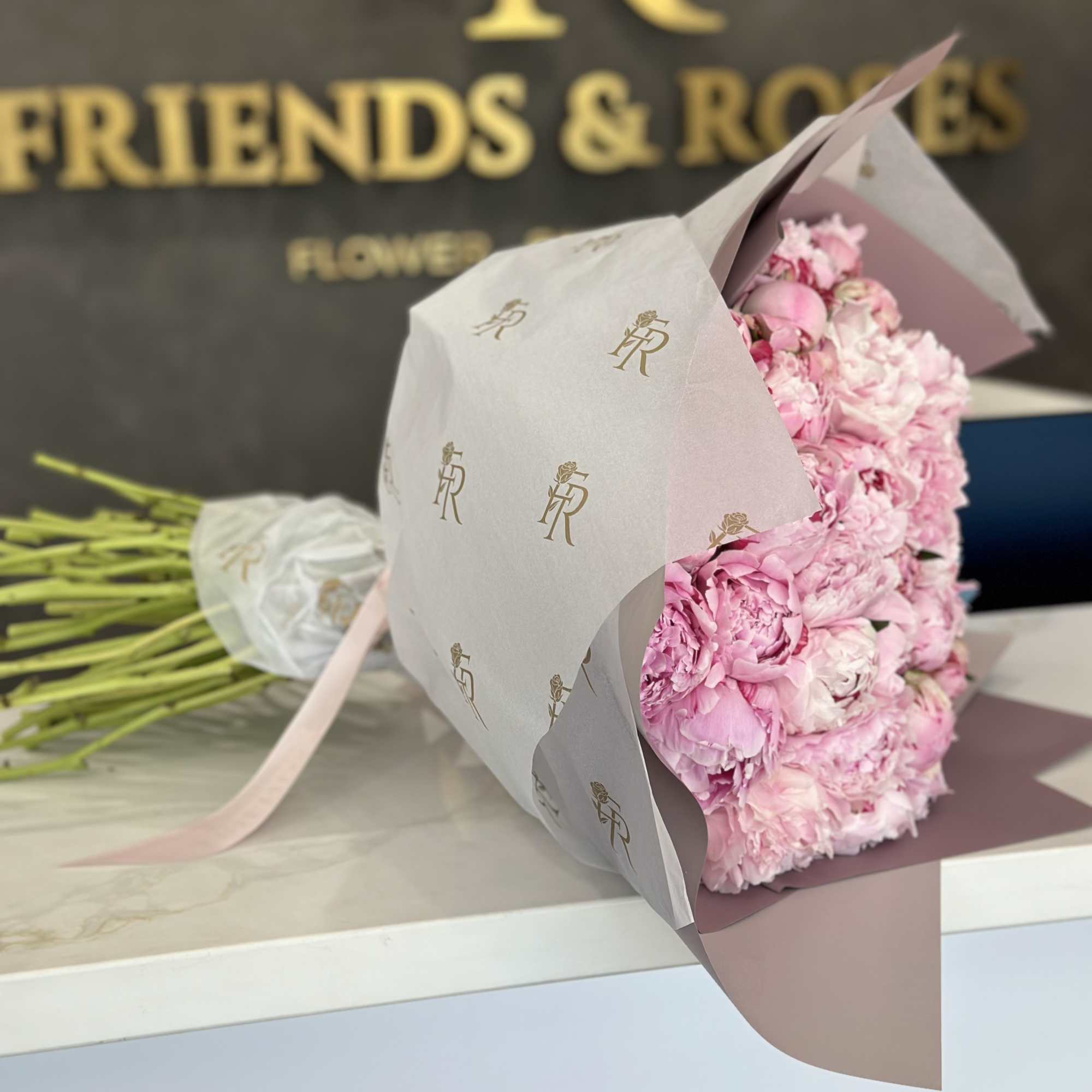 Pink peony bouquet wrapped in white paper with a pink ribbon
