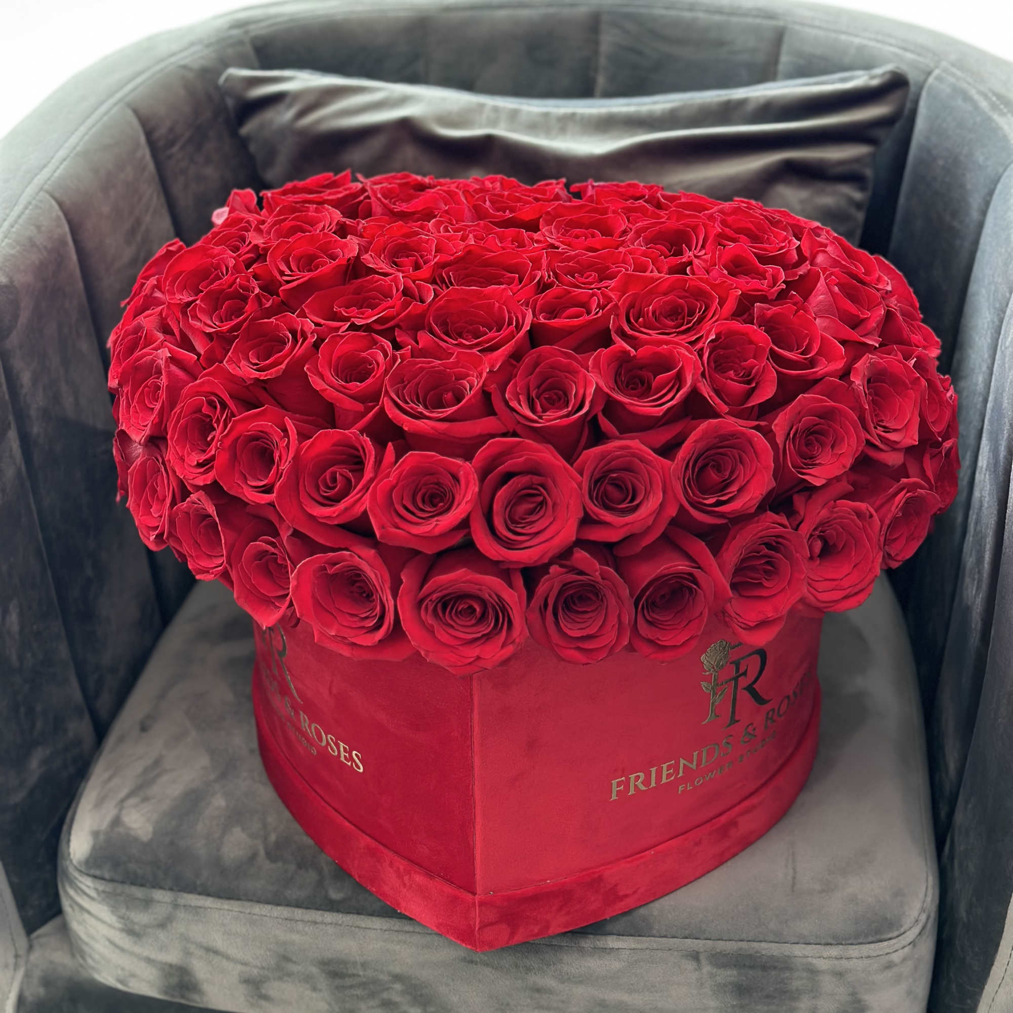 Heart-shaped box filled with red roses on a chair