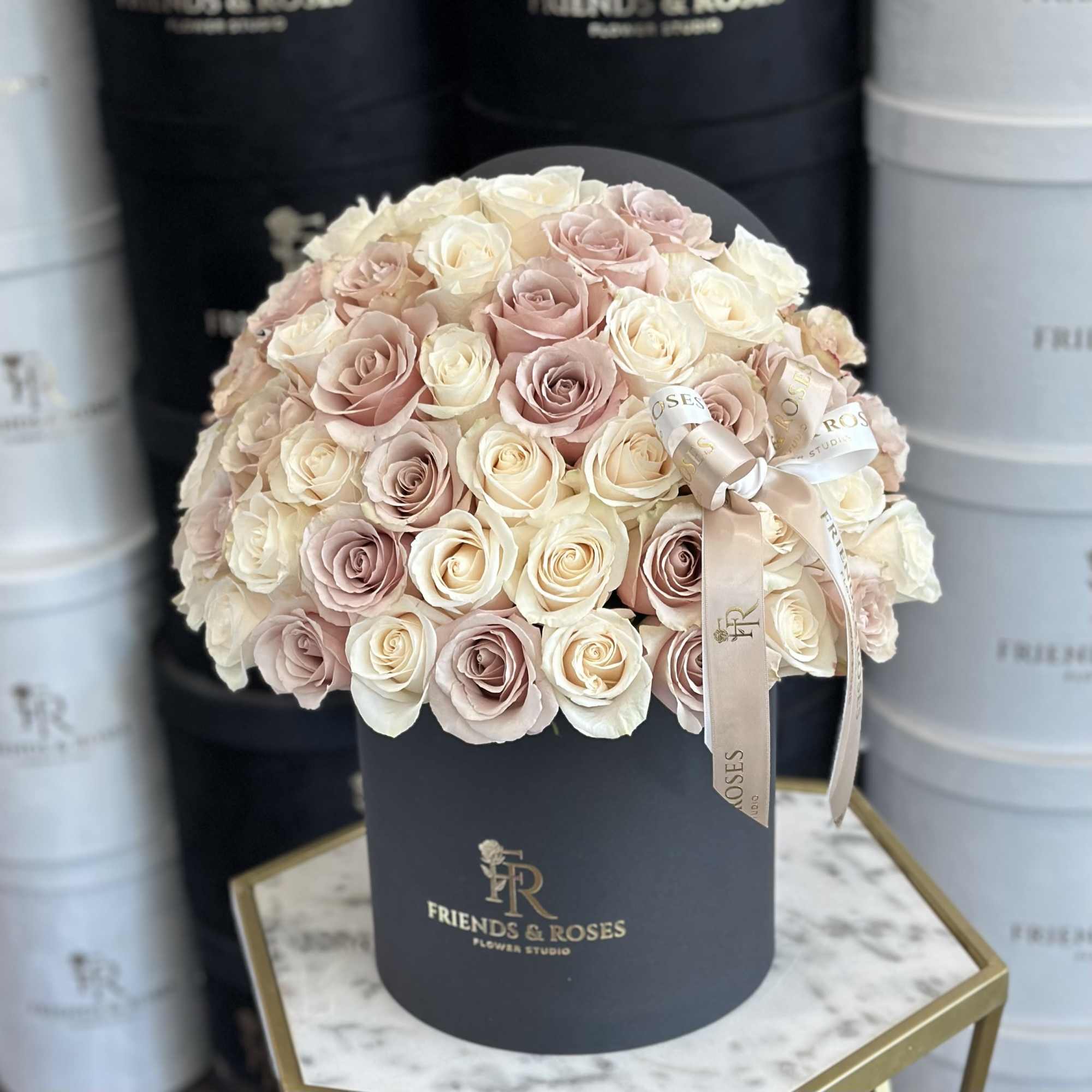 Round bouquet of blush and ivory roses in a black hat box with ribbon