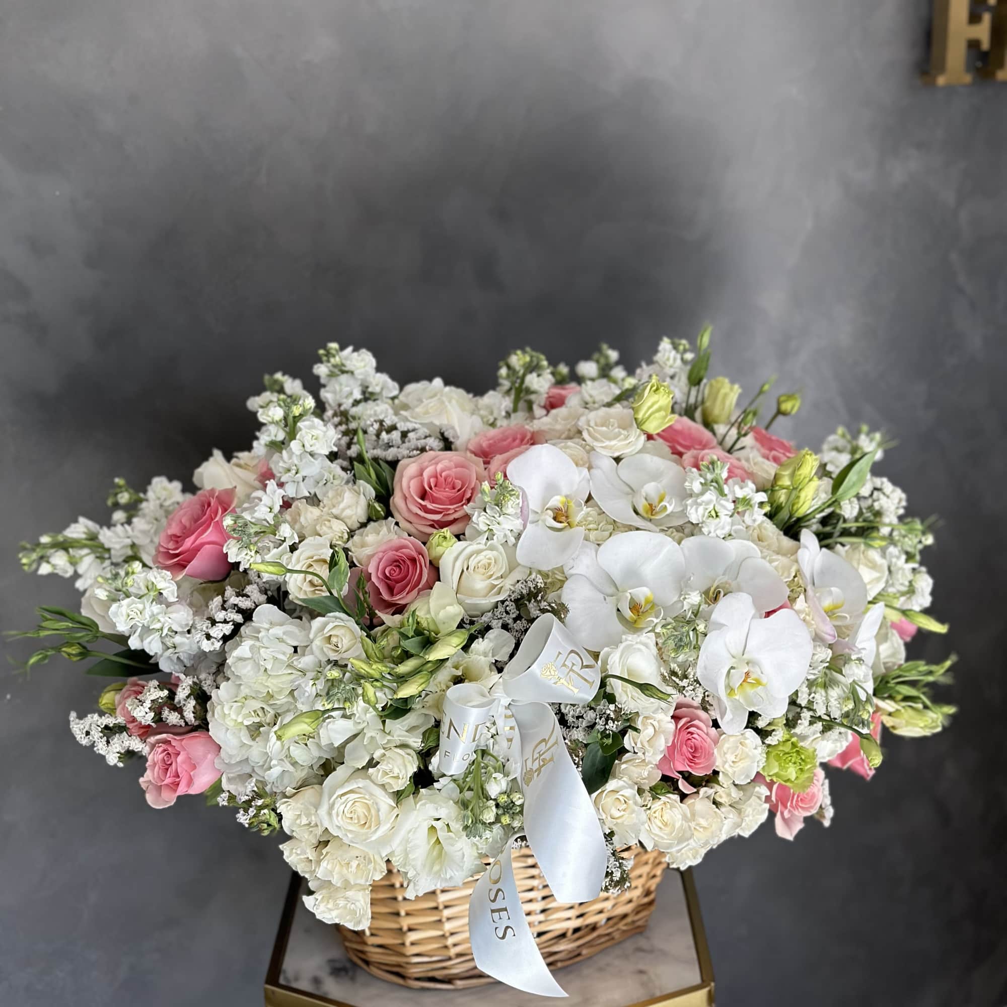 Basket arrangement of pink and white roses, hydrangeas, and white orchids with a ribbon