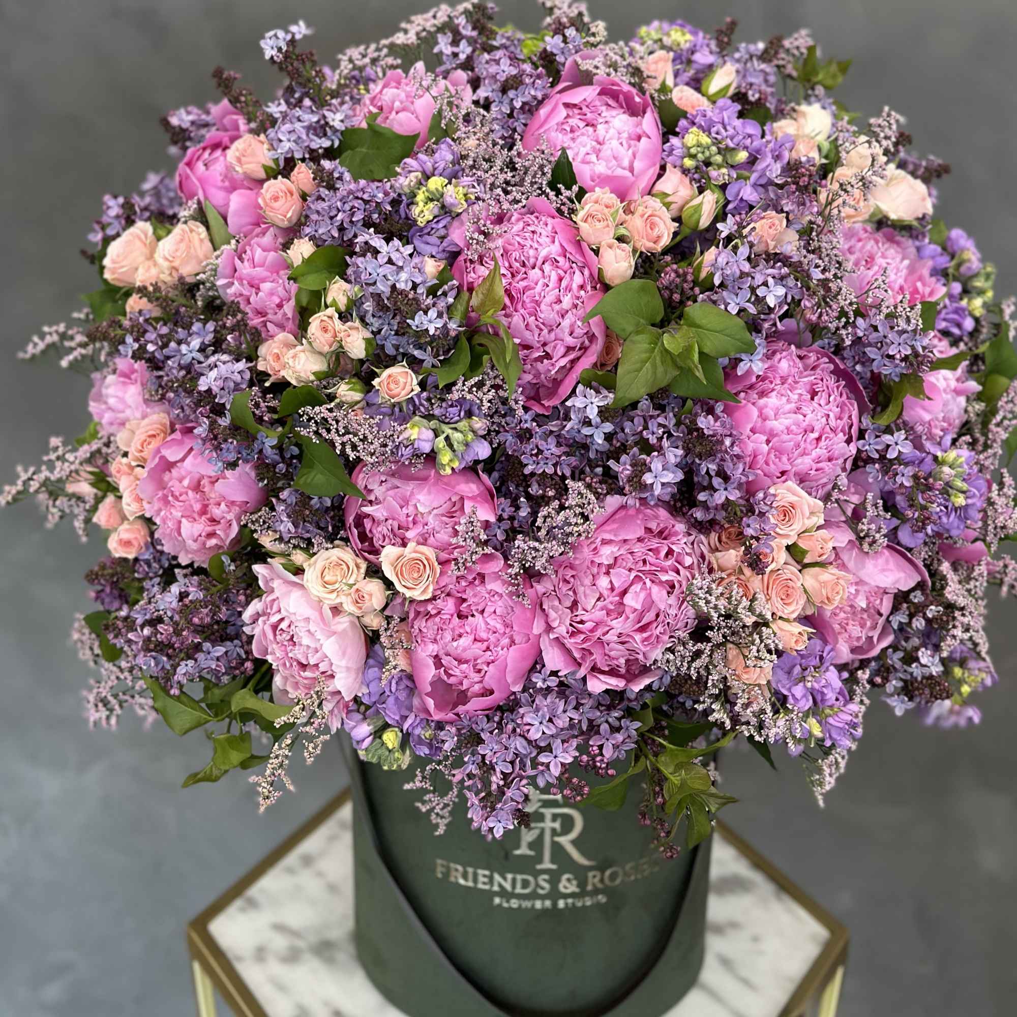 Pink peonies and lavender flowers in a dark green hat box