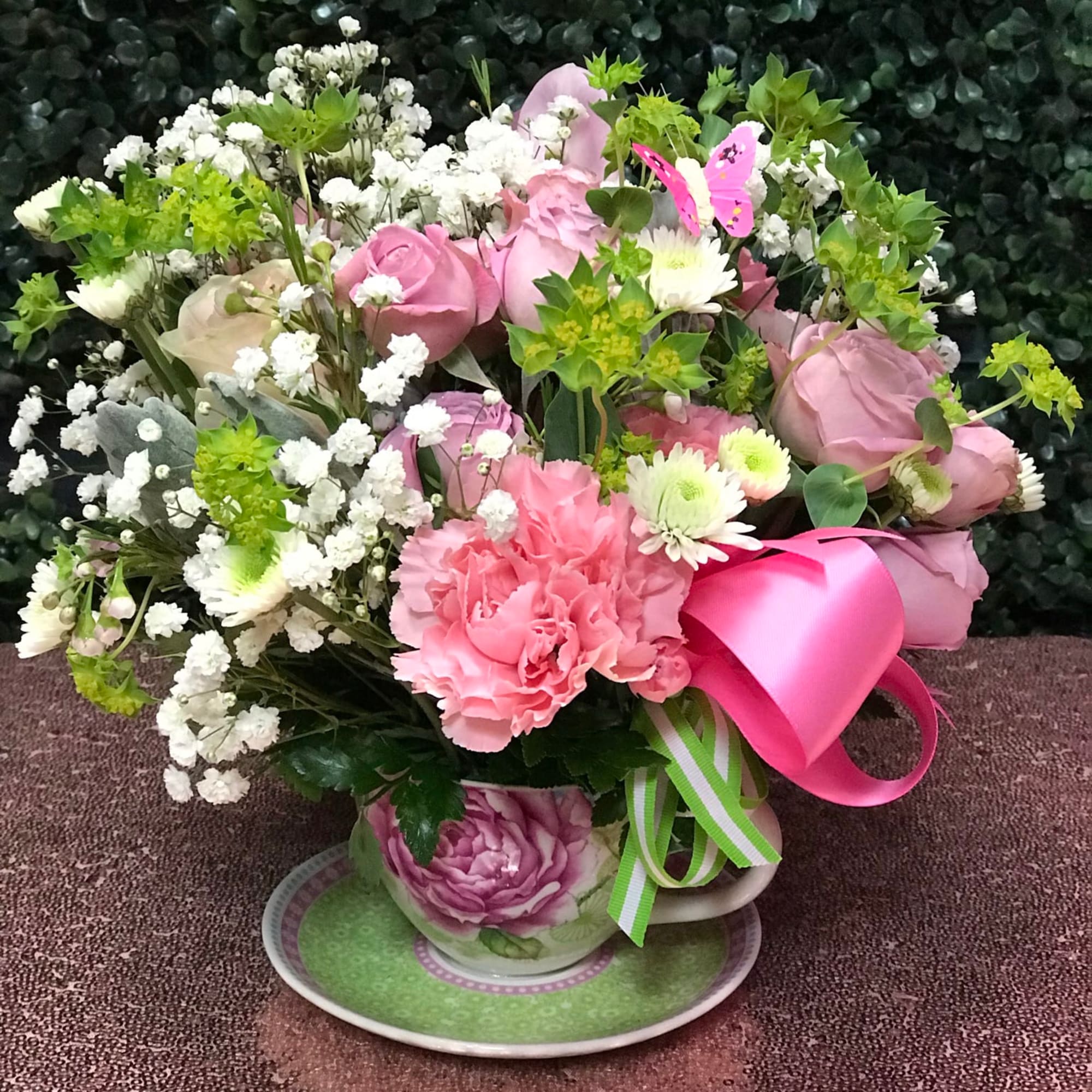 Pink rose bouquet with white filler flowers in a teacup vase