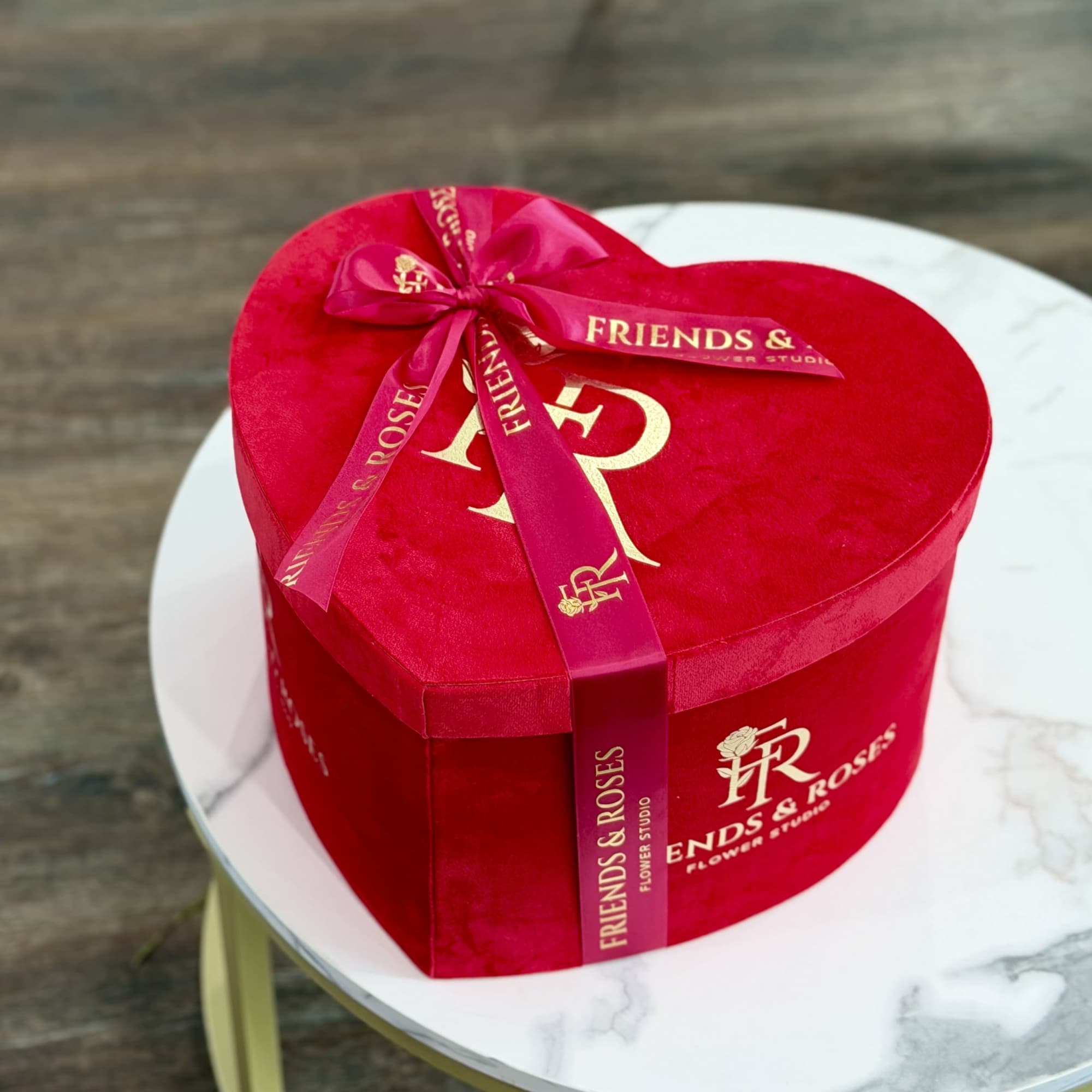 Heart-shaped red gift box with a ribbon on a round table