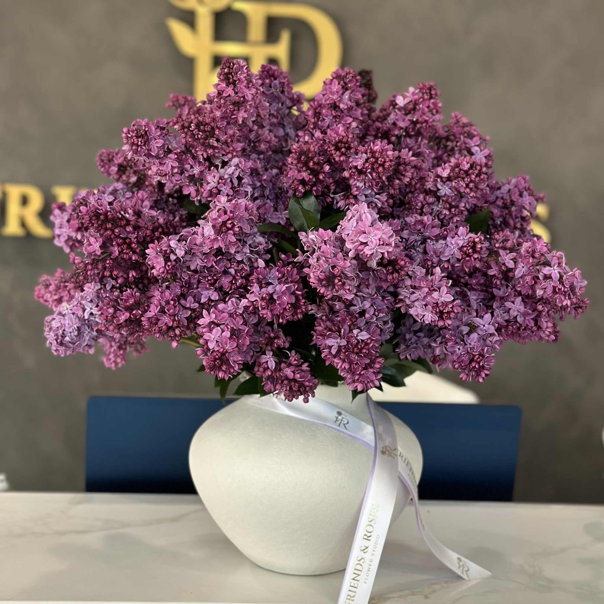 Purple lilac bouquet in a white vase with a ribbon