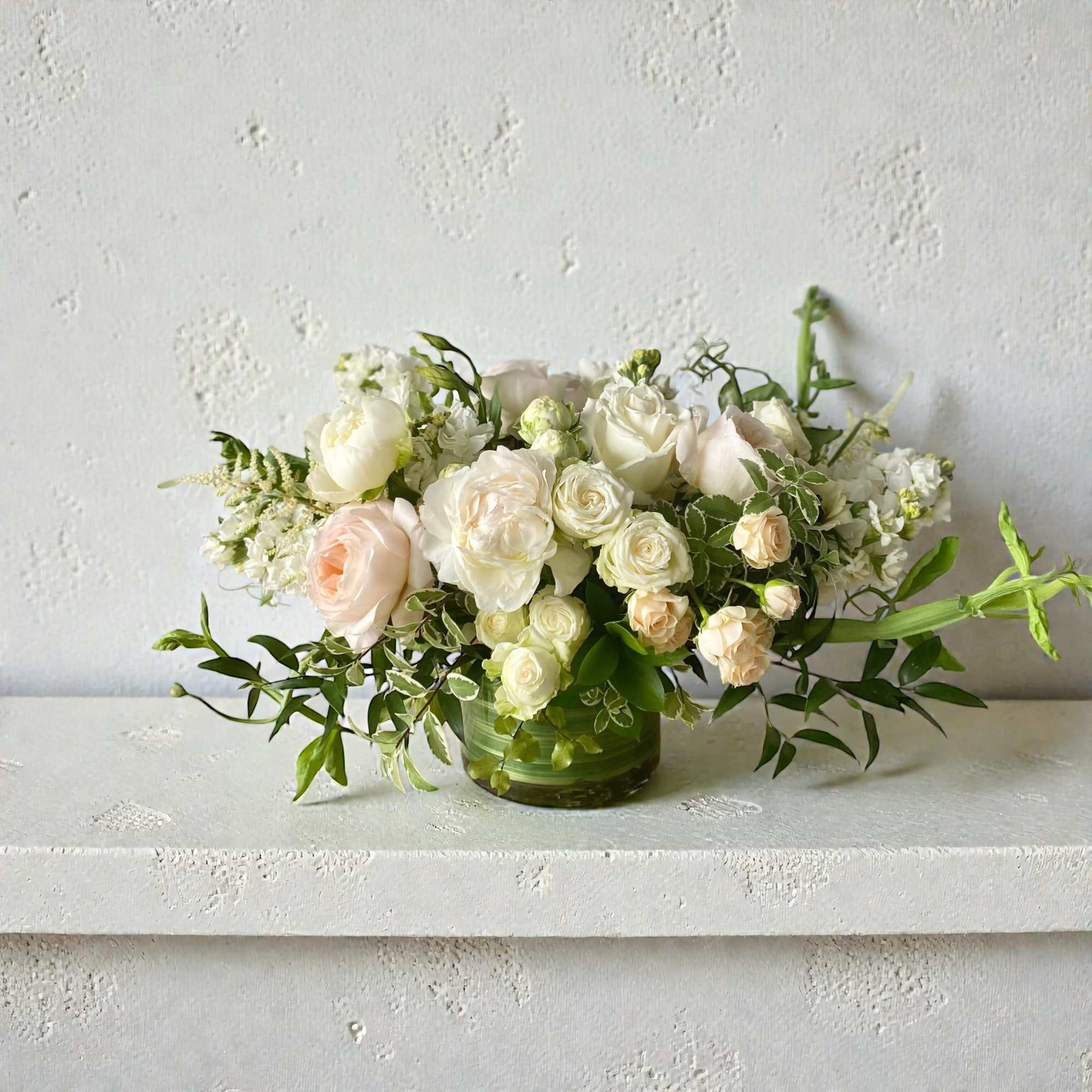 White and blush roses arranged in a green glass vase
