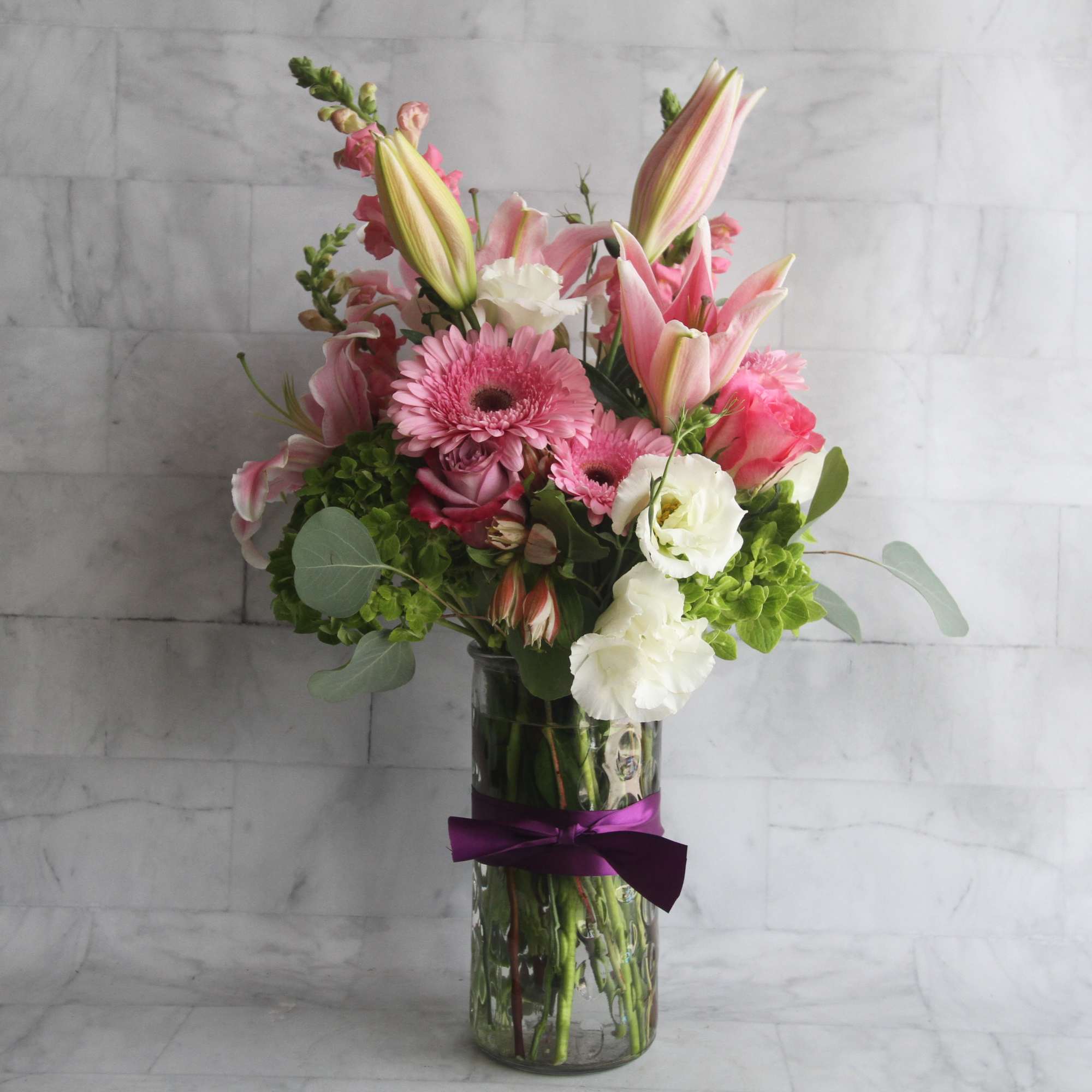 Pink and white mixed bouquet in a glass vase with a purple ribbon