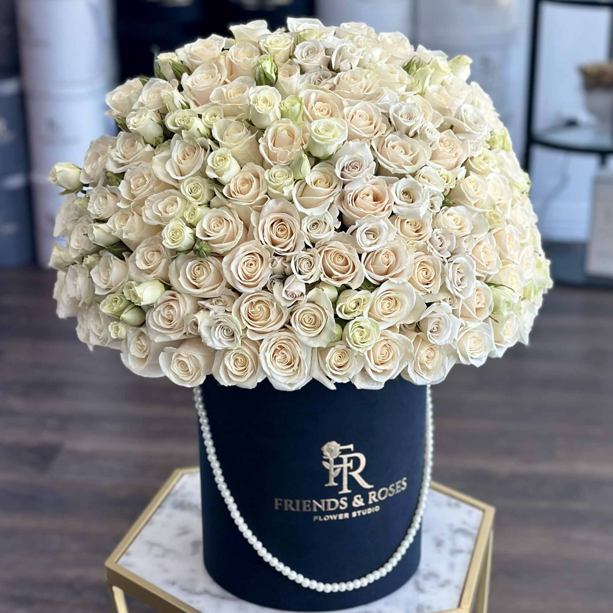 Large cream rose arrangement in a navy hat box with pearl trim