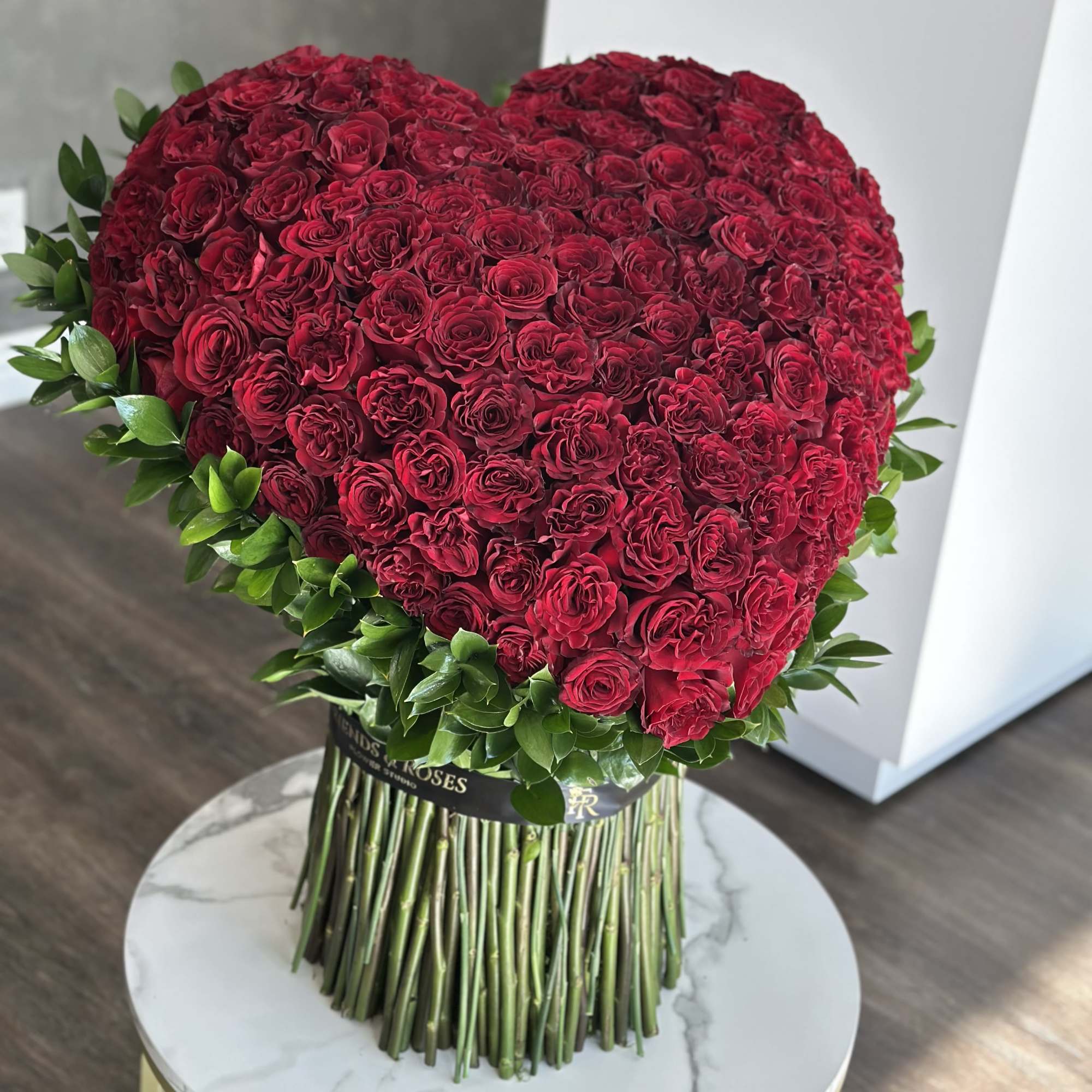 Heart-shaped bouquet of red roses with green leaves and long stems