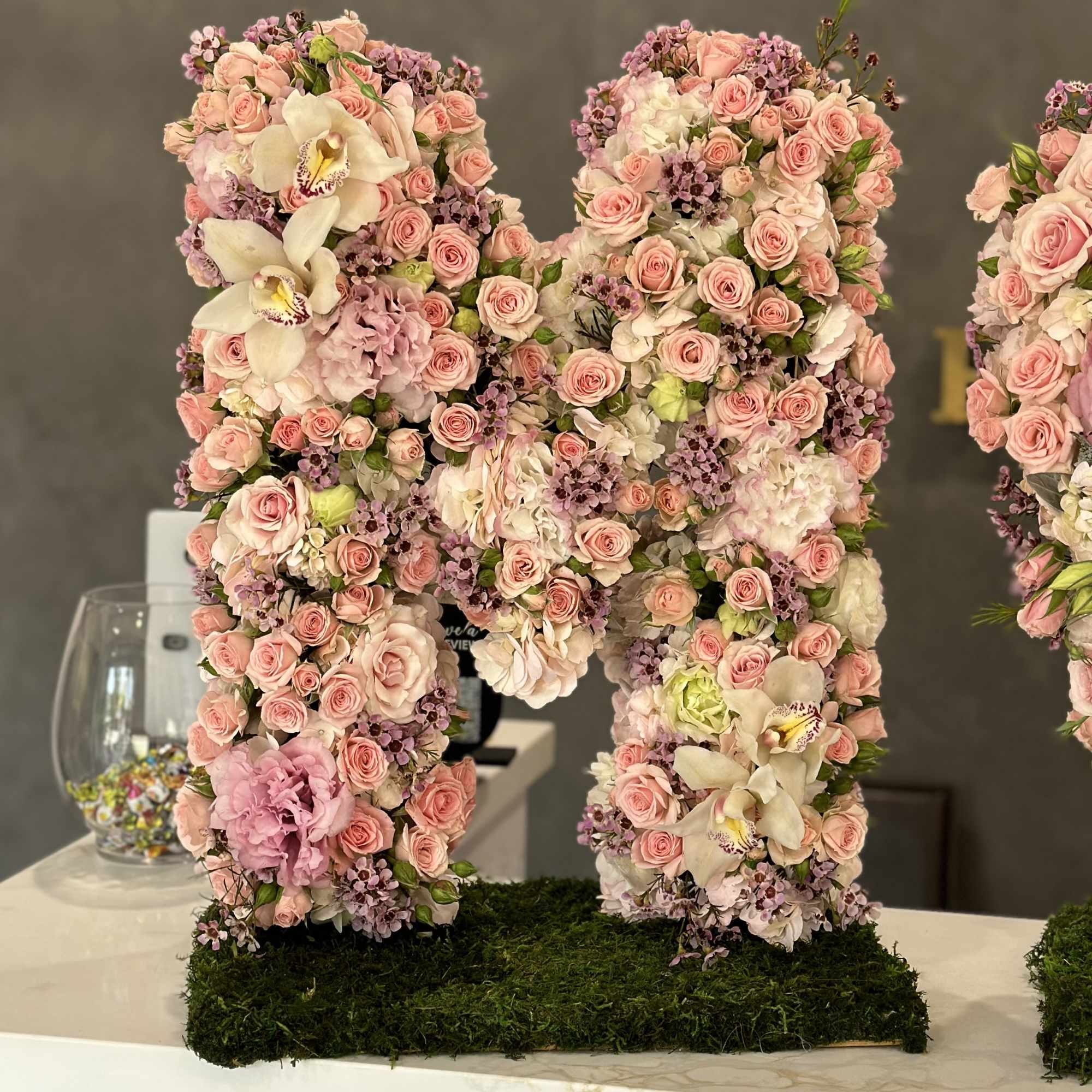 Large floral letter covered in pink roses and orchids on a moss base.