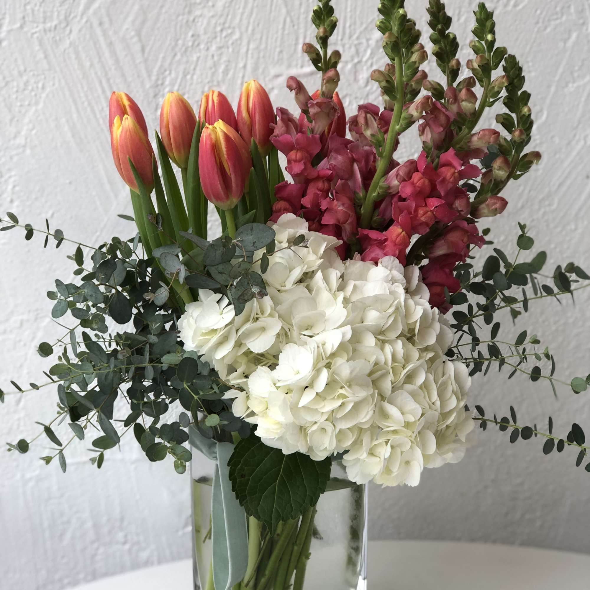 Bouquet of pink tulips, white hydrangeas, and magenta snapdragons in a glass vase