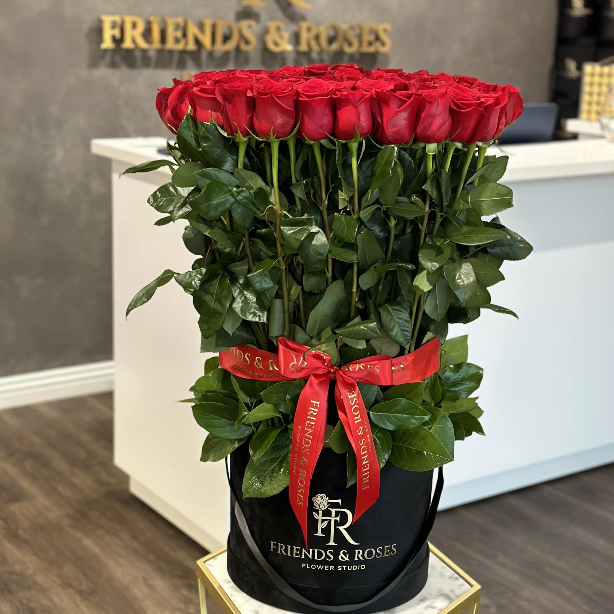 Tall bouquet of red roses in a black hatbox with a red ribbon