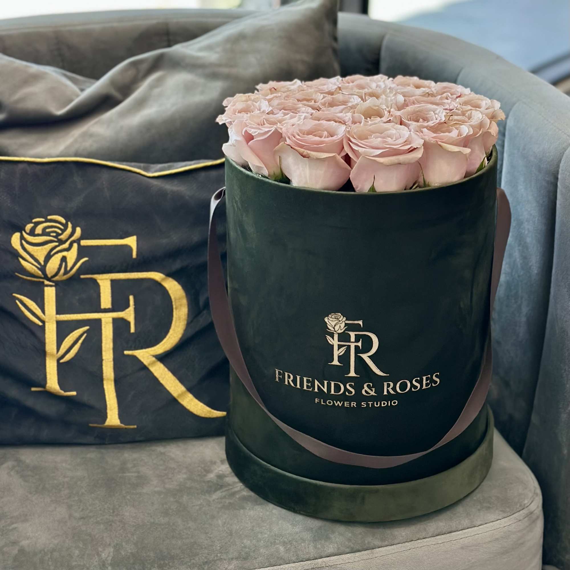 Pink roses arranged in a dark green round box on a sofa