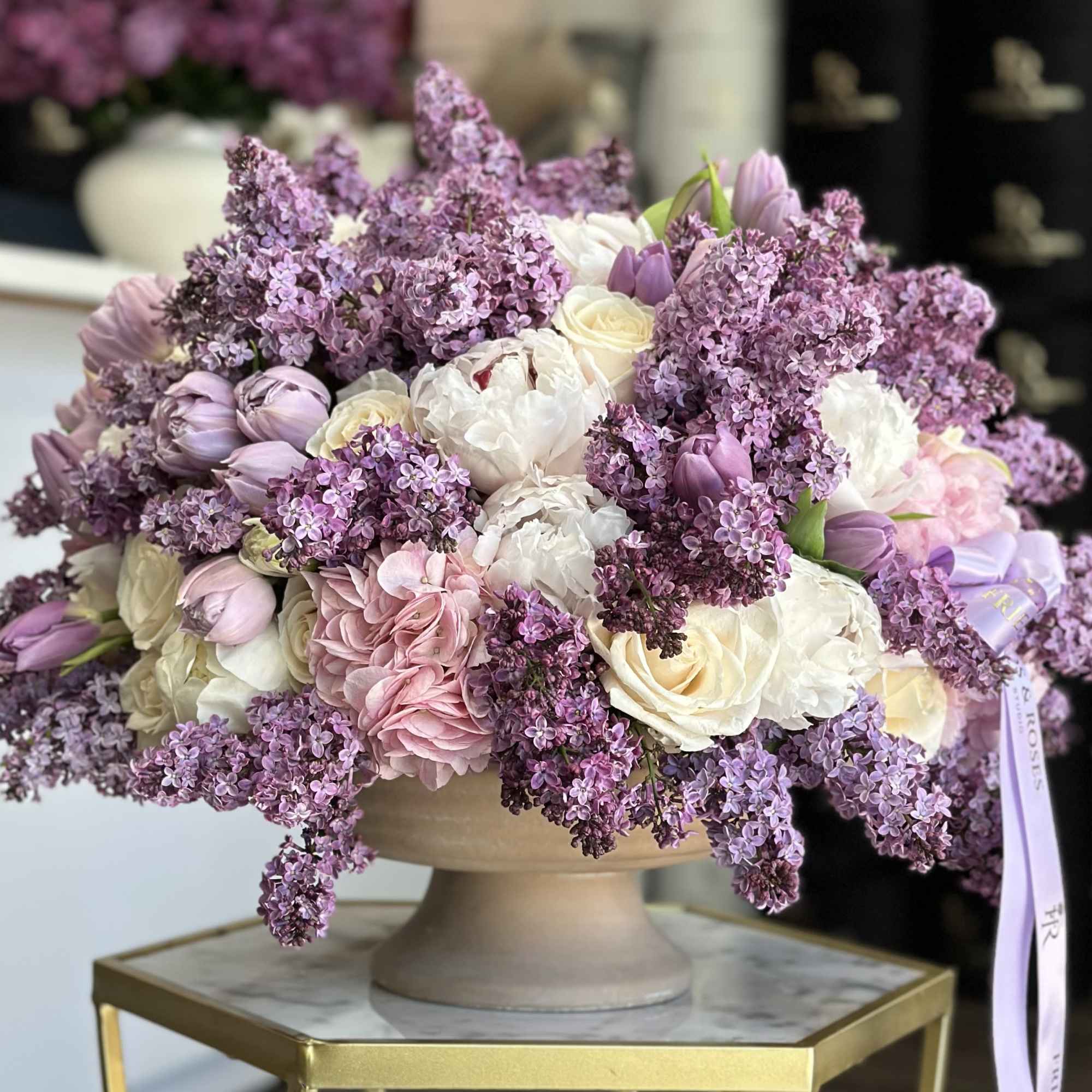 Lavender and white floral arrangement in a pedestal bowl with a ribbon