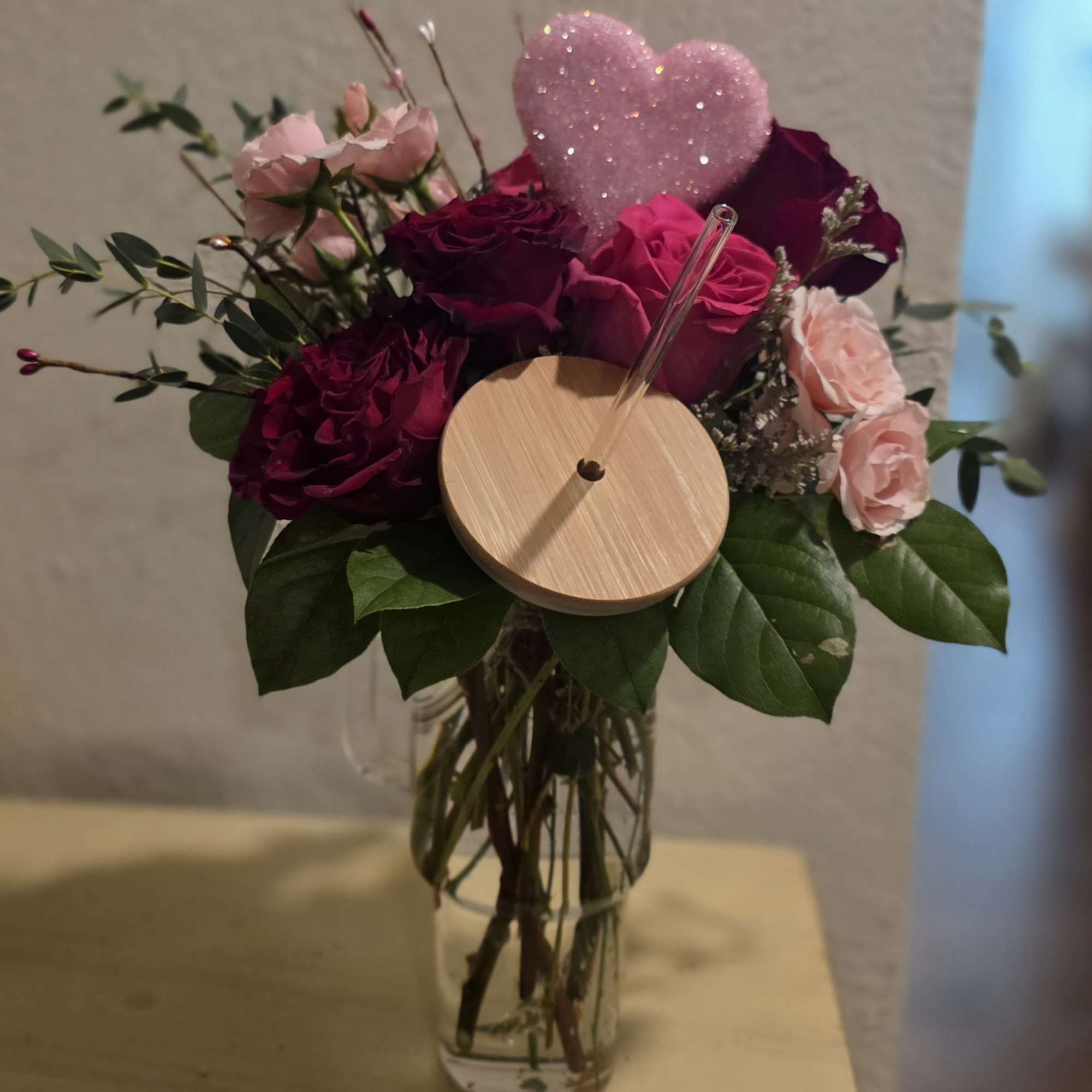 Pink and burgundy roses in a clear vase with a glittery heart pick