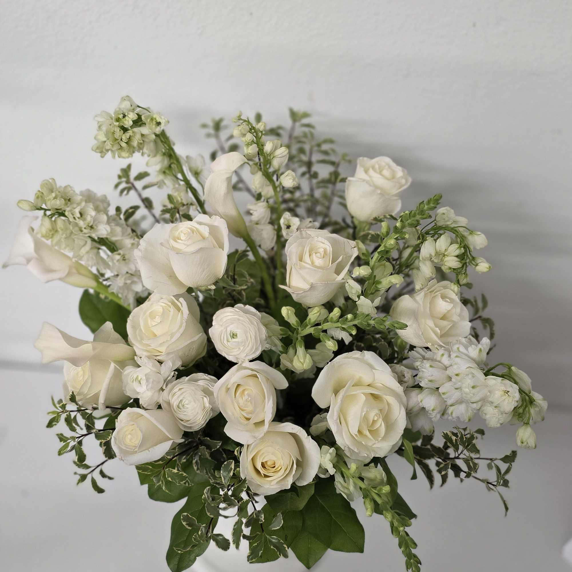 White roses and calla lilies arranged in a white vase