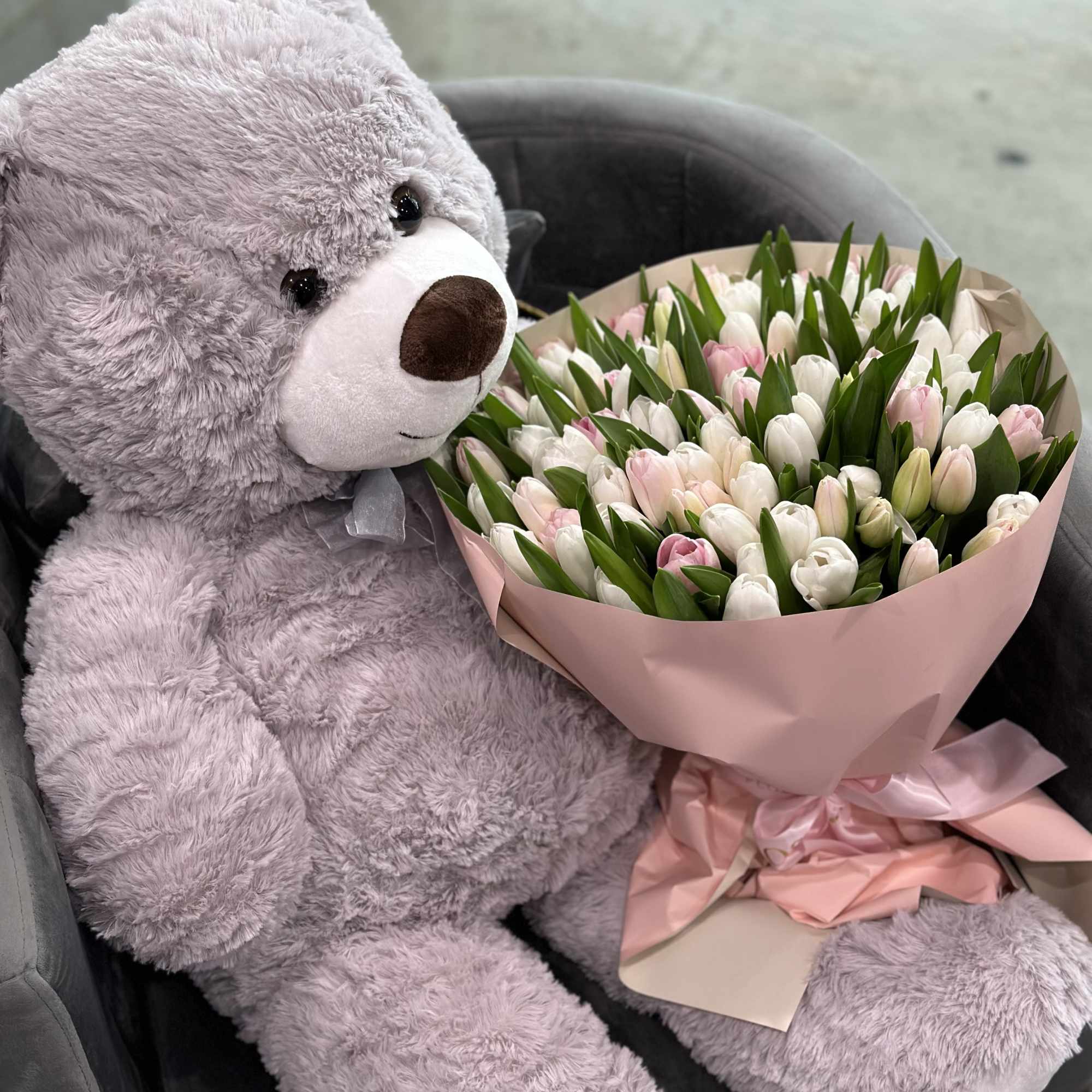 Lavender teddy bear beside a bouquet of pink and white tulips