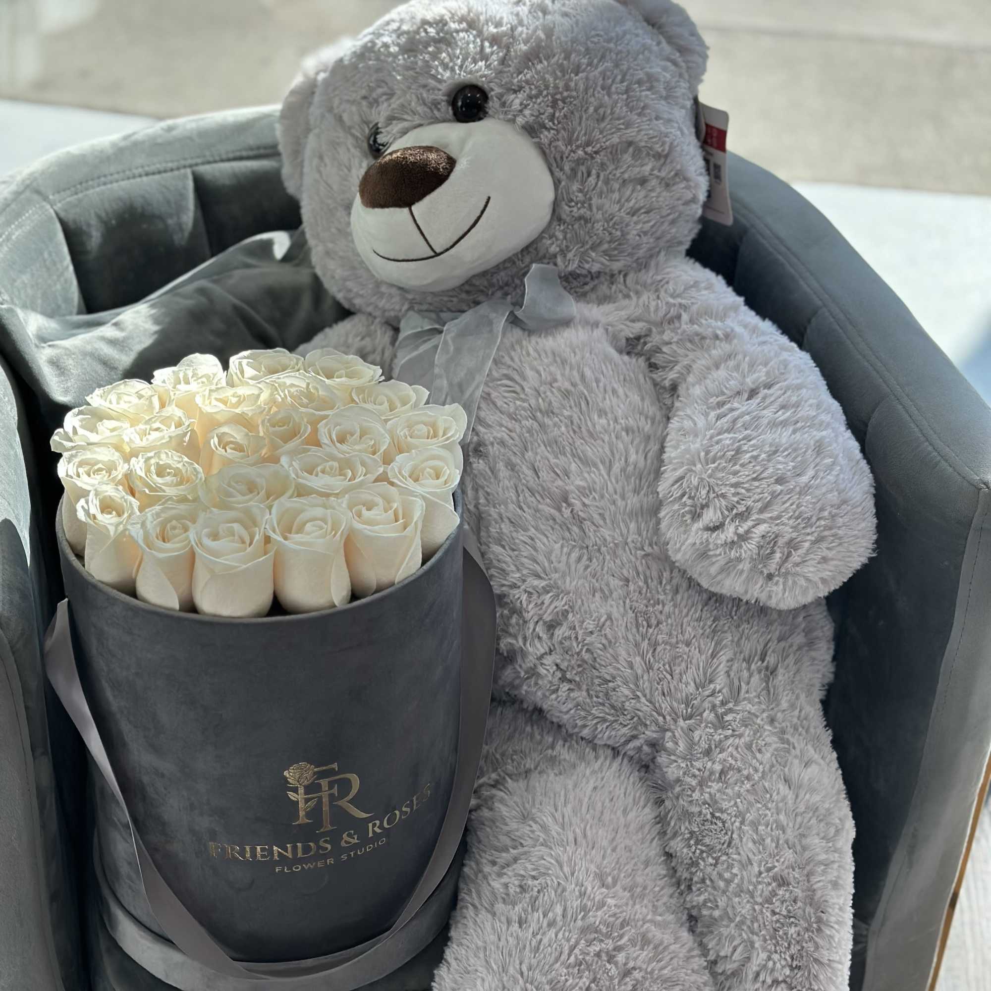 Cream roses in a black box beside a gray teddy bear