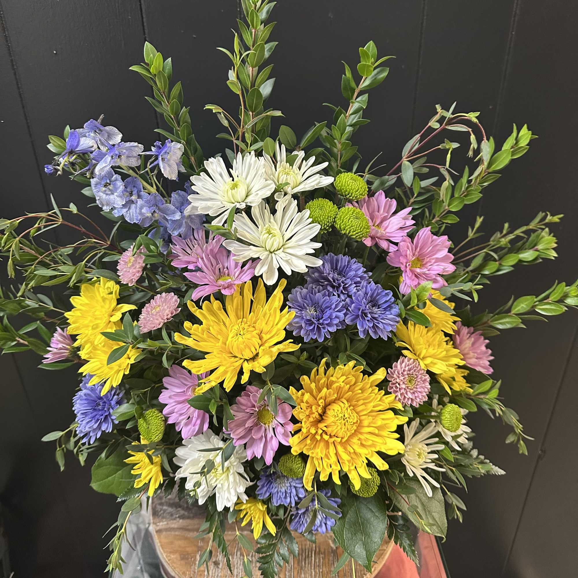 Bright mix of chrysanthemums and daisies arranged in a small sympathy urn