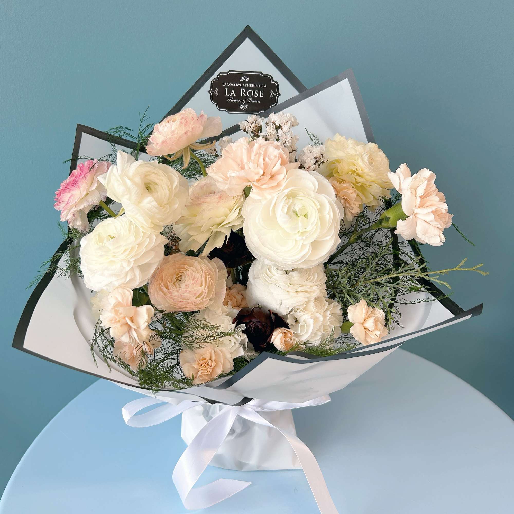 Bouquet of pale pink and white flowers wrapped in white paper with a ribbon