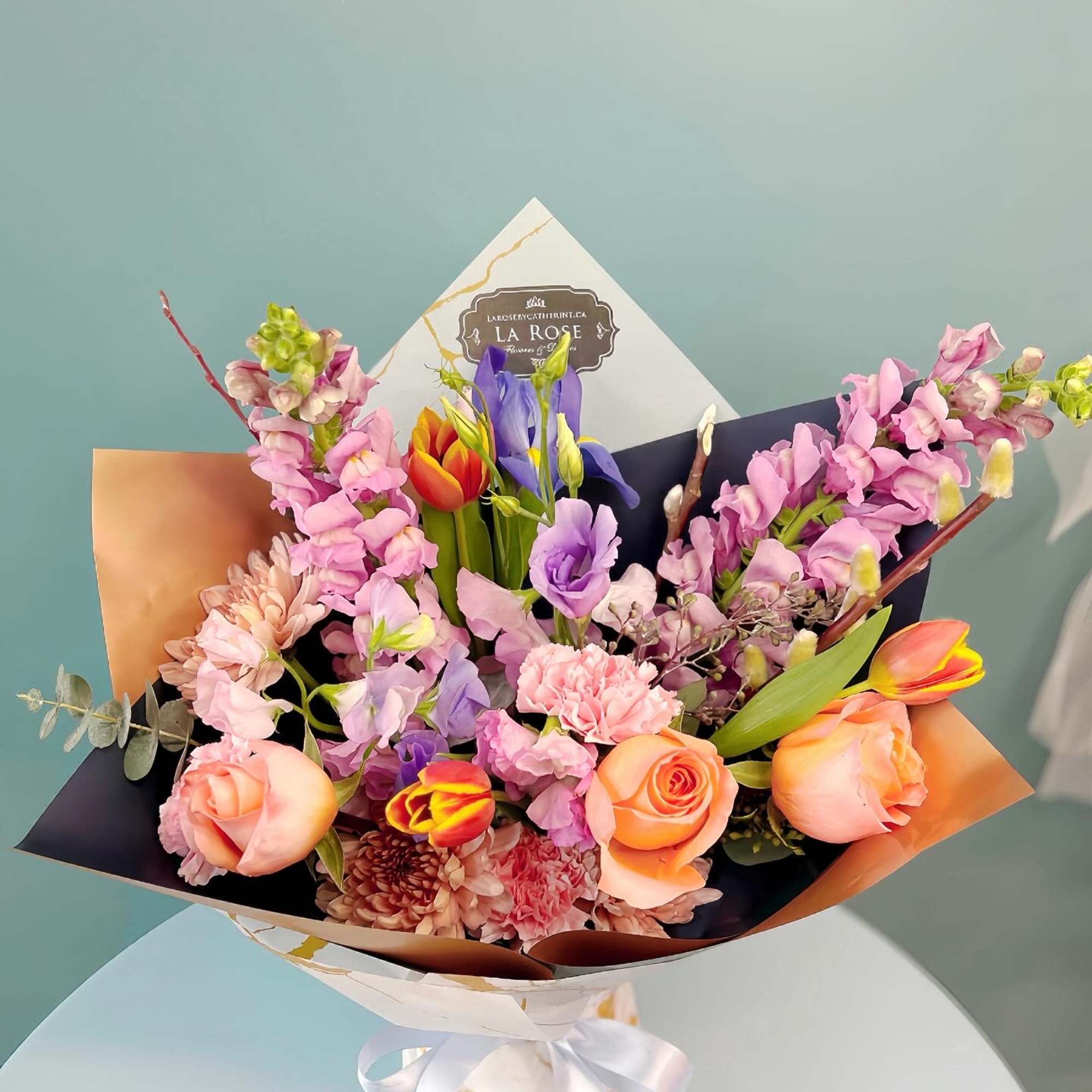 Bouquet of peach roses, pink blooms, and purple flowers wrapped in paper