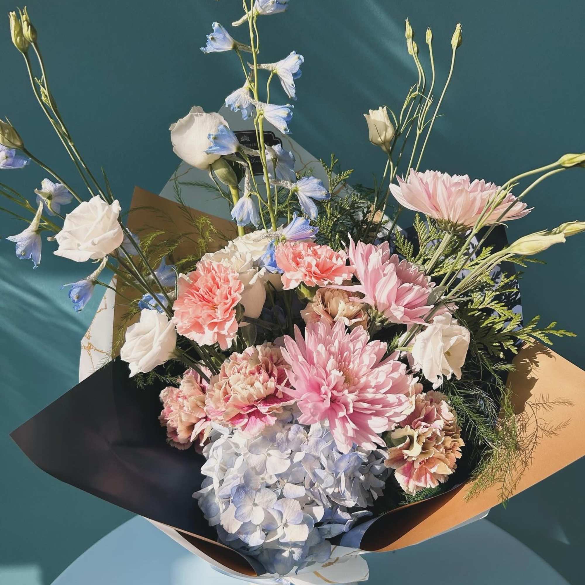 Bouquet of pink, white, and blue flowers wrapped in dark paper