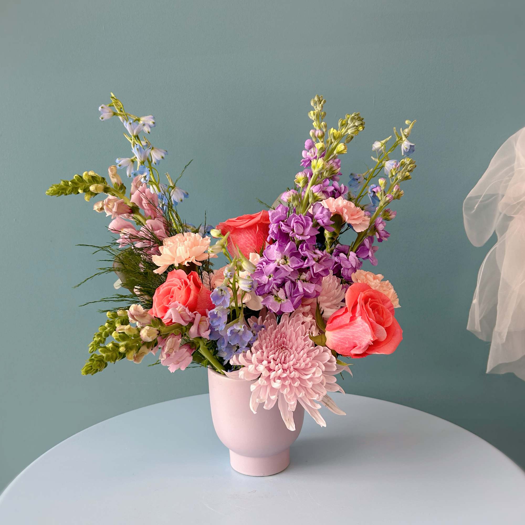 Mixed bouquet of pink, purple, and coral flowers in a pale pink vase