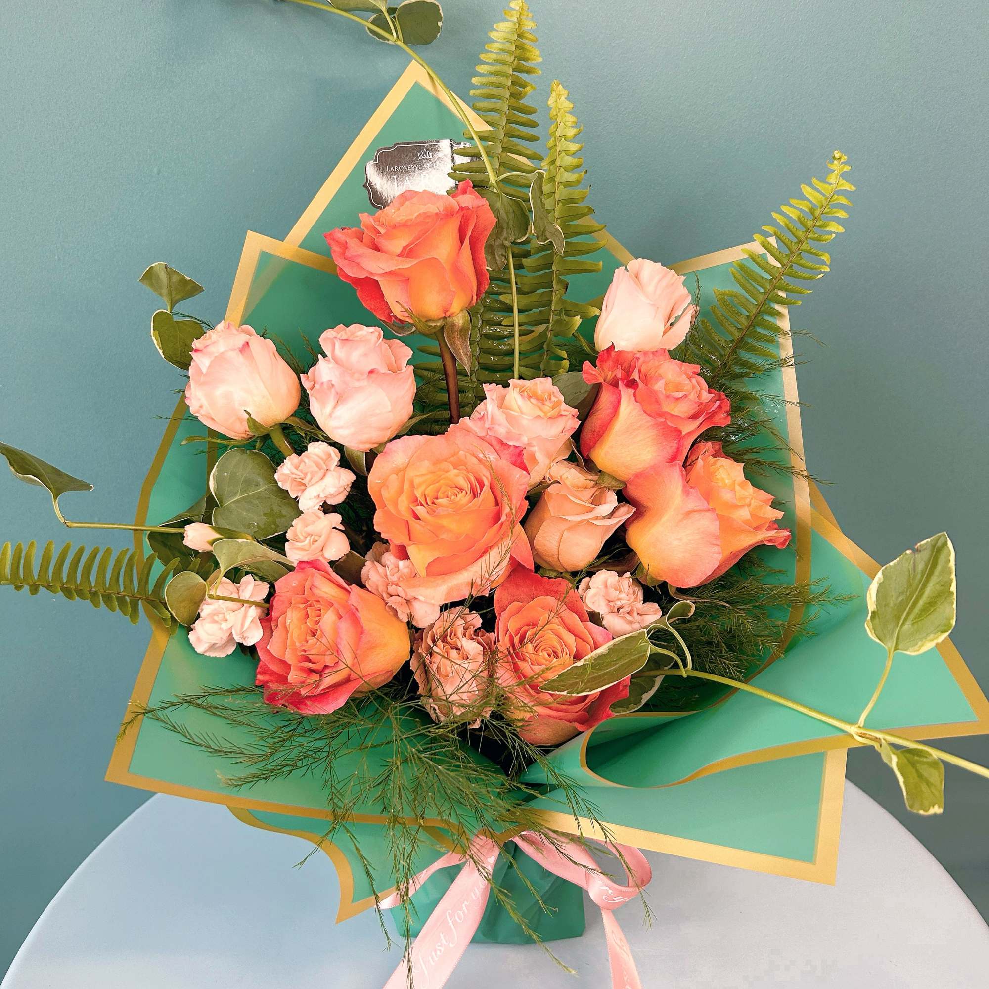 Bouquet of peach and pink roses with greenery in teal wrap
