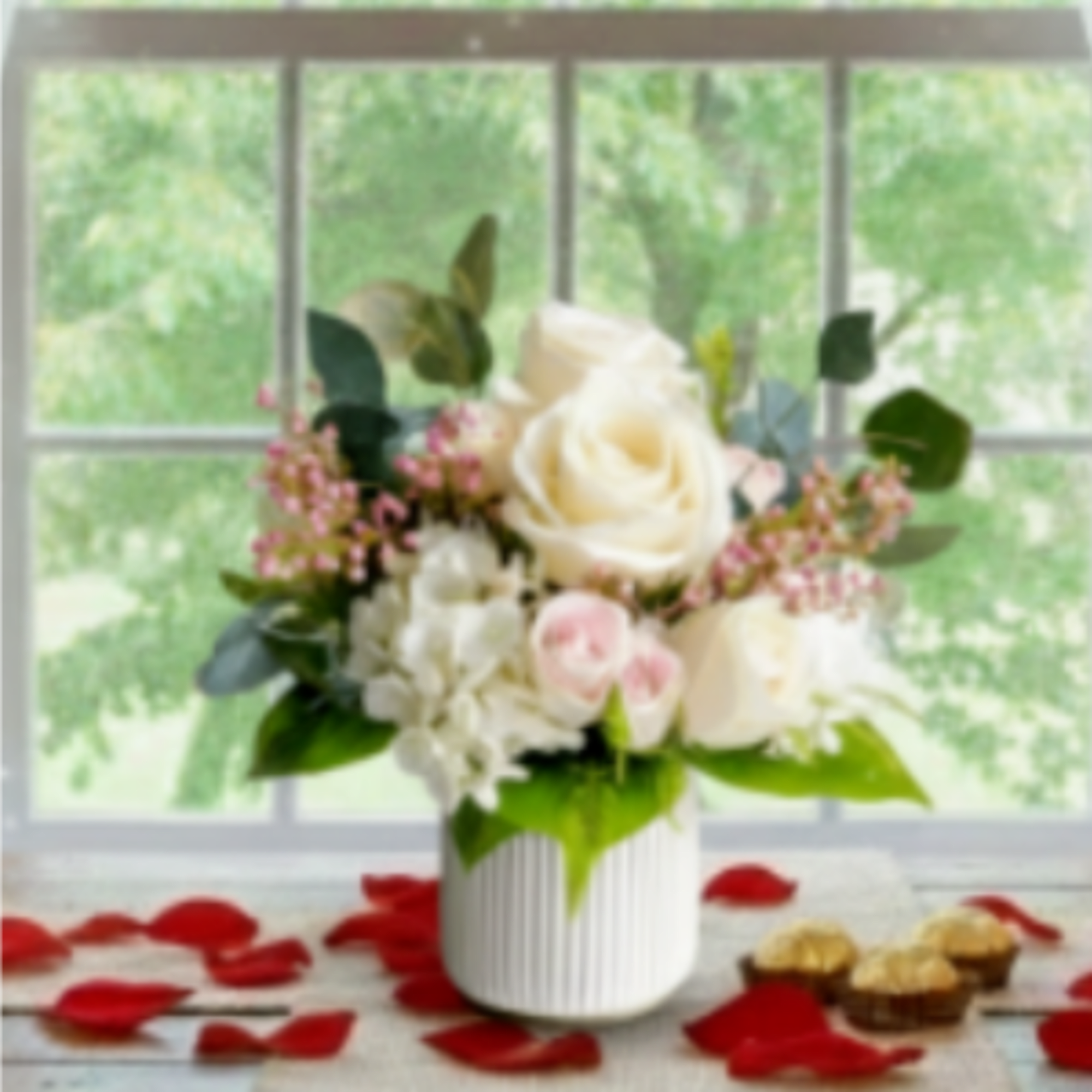 White and blush roses in a ribbed vase with red petals around it