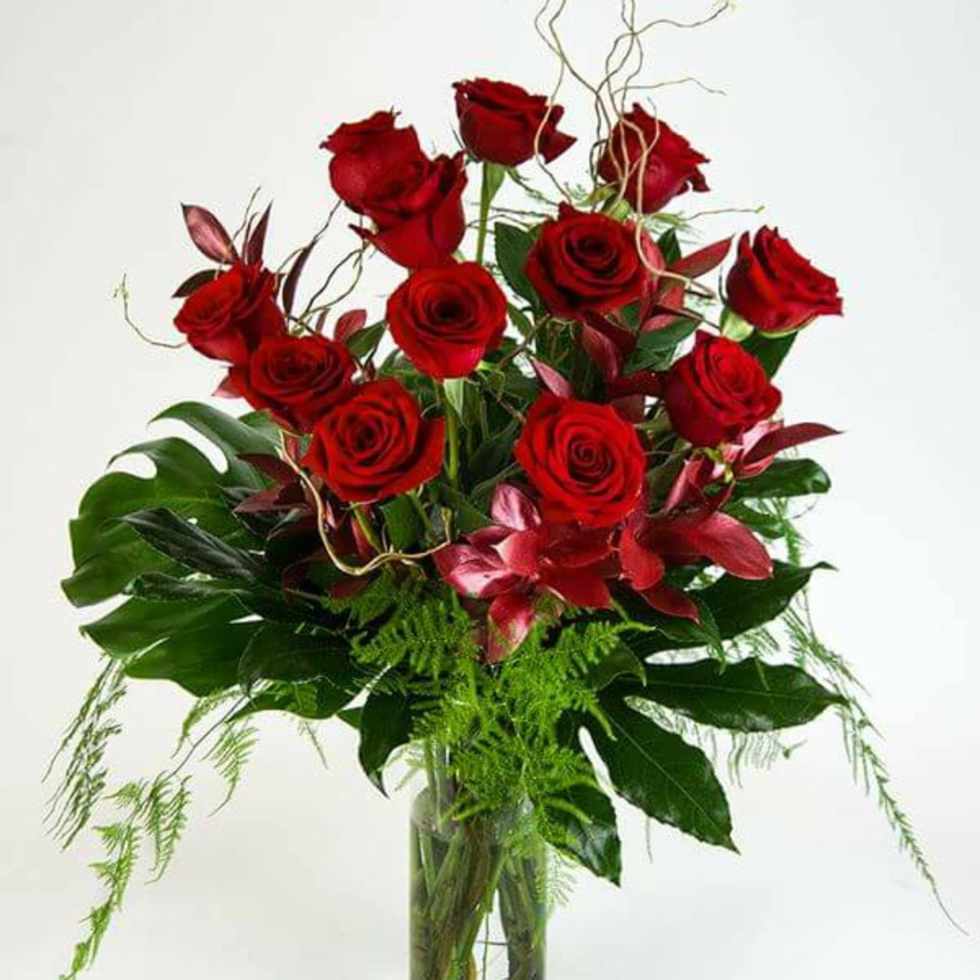 Red roses arranged in a clear glass vase with tropical foliage