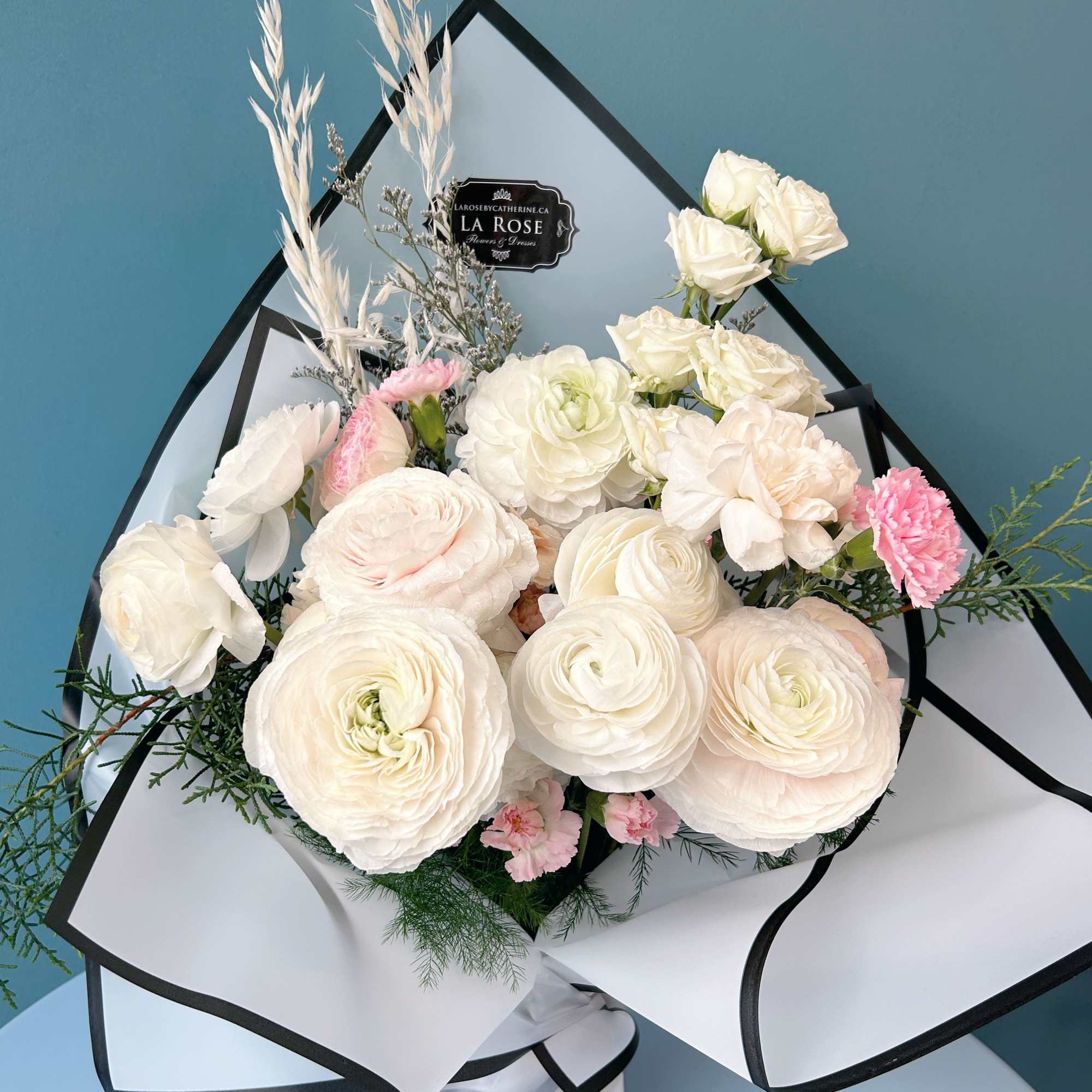 Bouquet of white and blush flowers wrapped in white paper with black trim