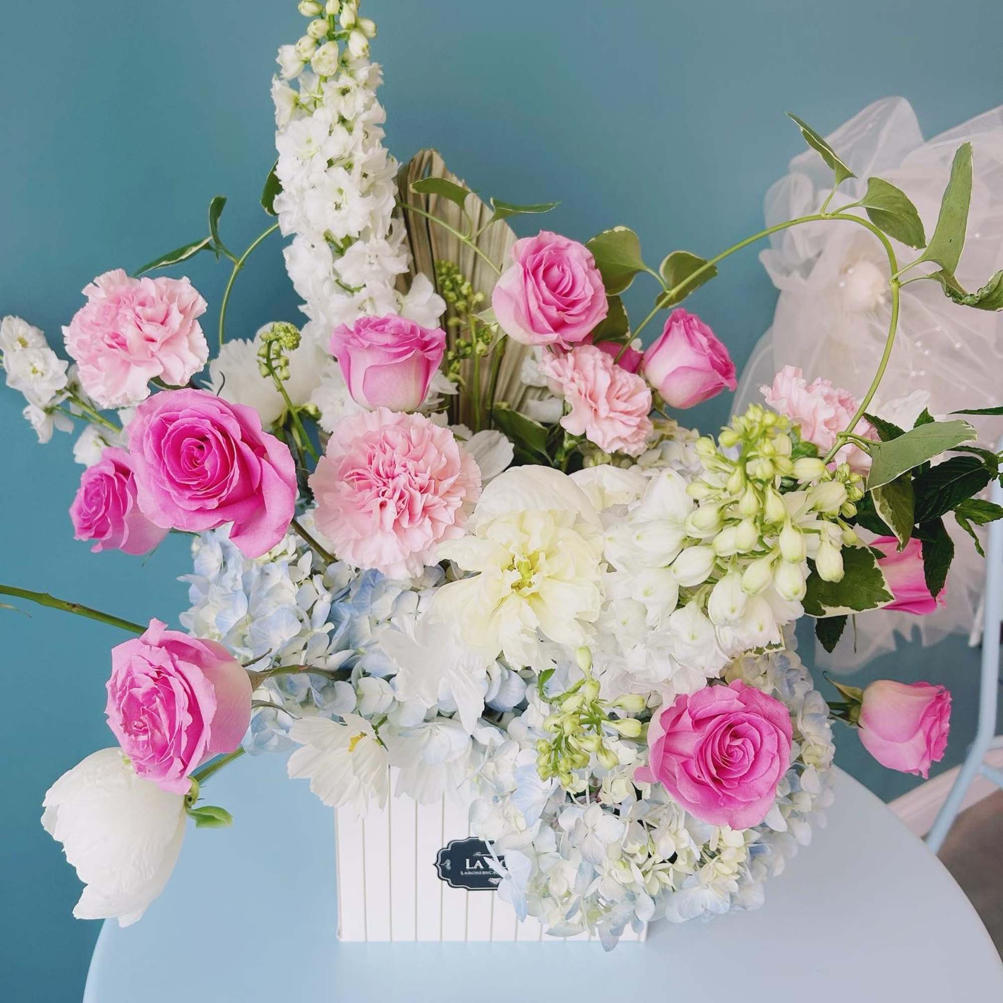 Pink roses and white flowers arranged in a white box
