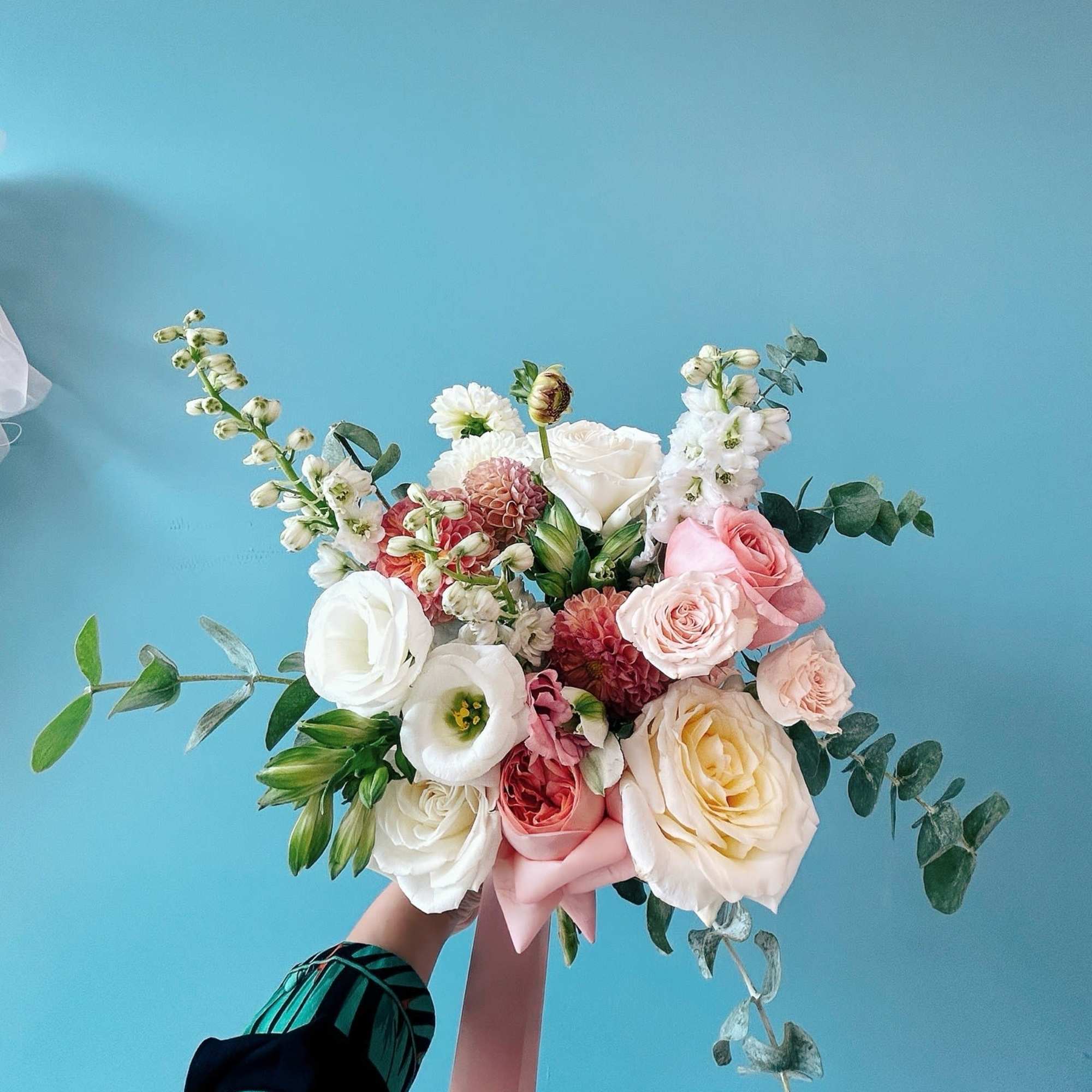 Handheld bouquet of white, pink, and cream flowers with trailing greenery