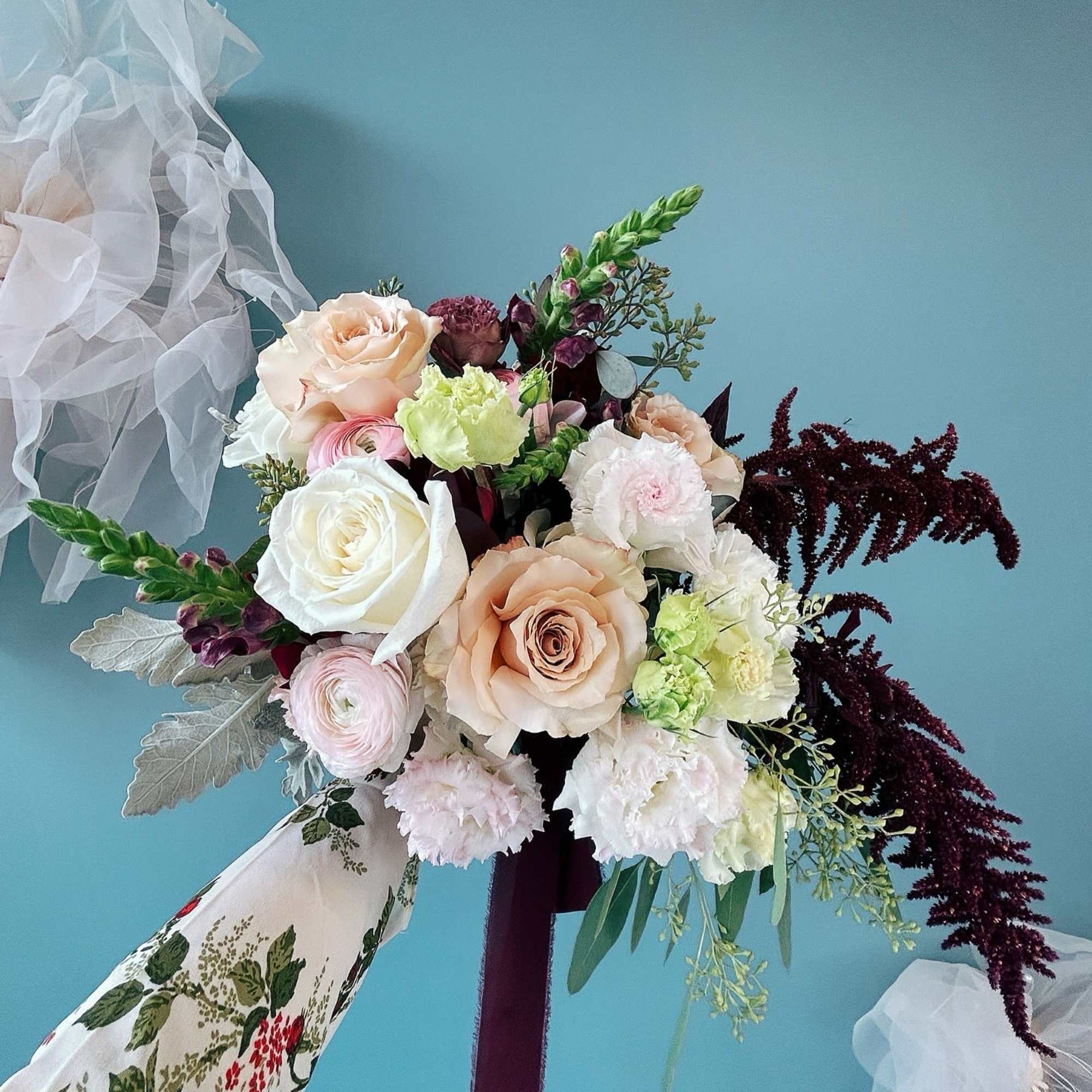 Wedding bouquet with blush, white, and burgundy flowers tied with ribbon