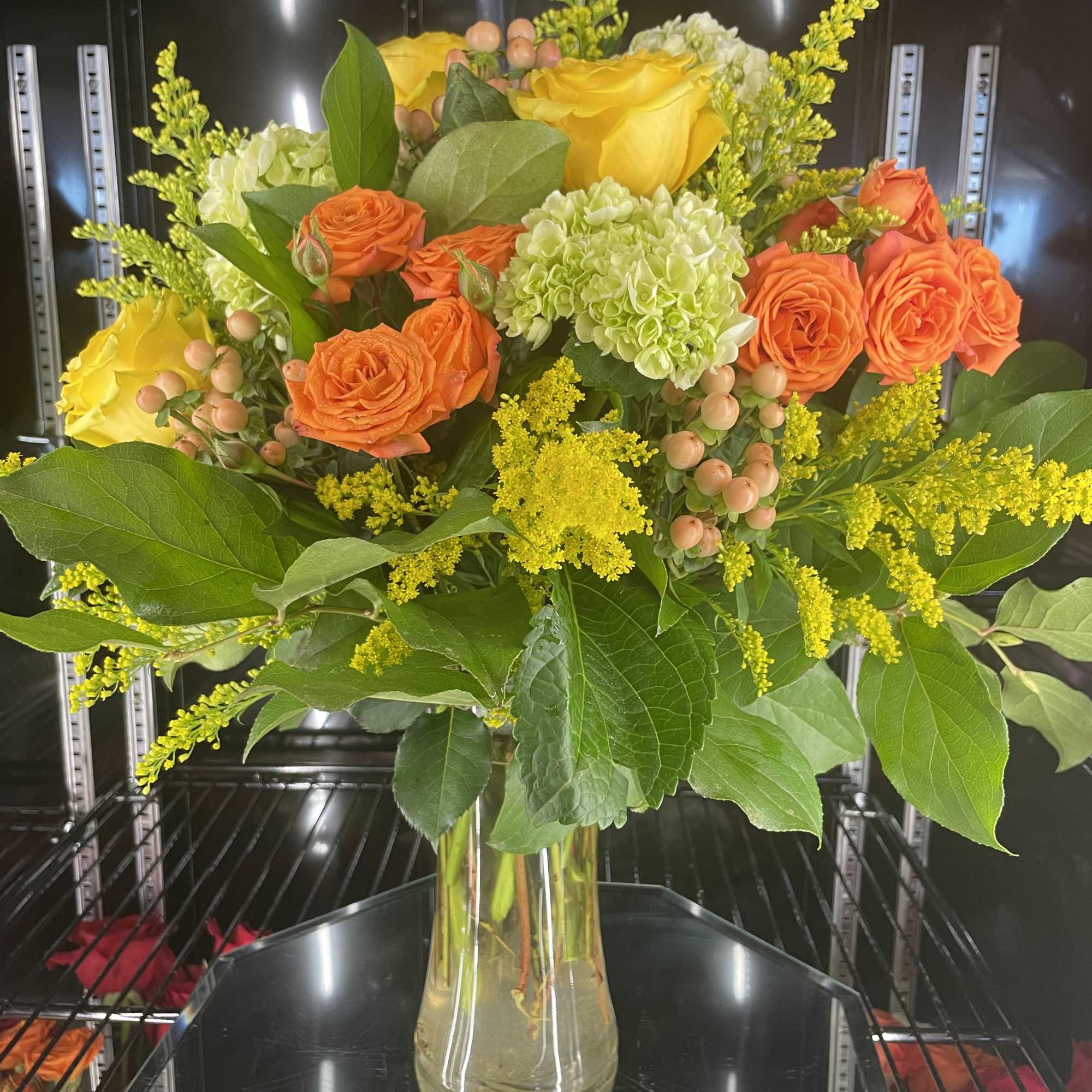 Bouquet of yellow and orange roses with green hydrangeas in a glass vase