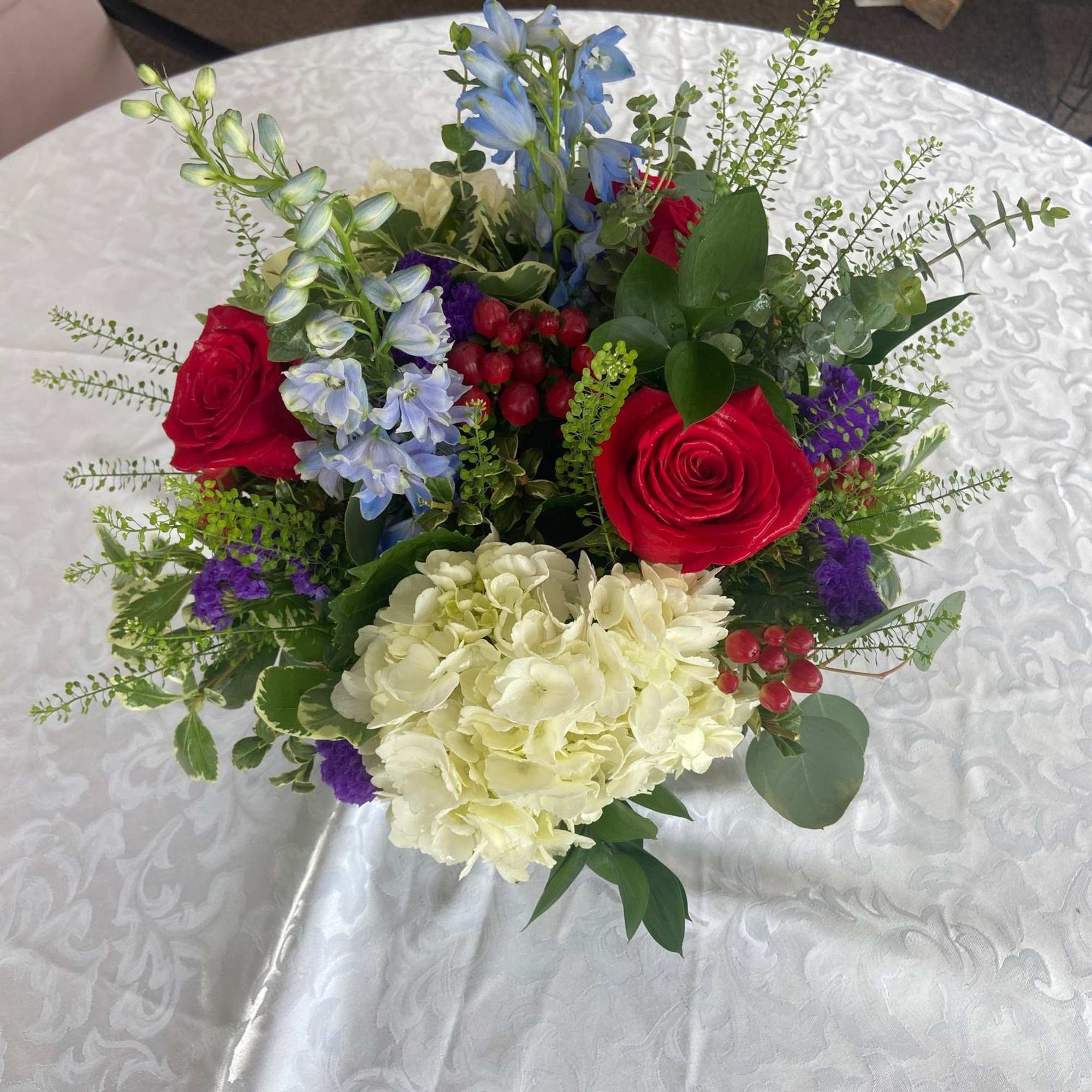 A beautiful mix of roses, delphinium, hydrangea, statice, and hypericum berries. This